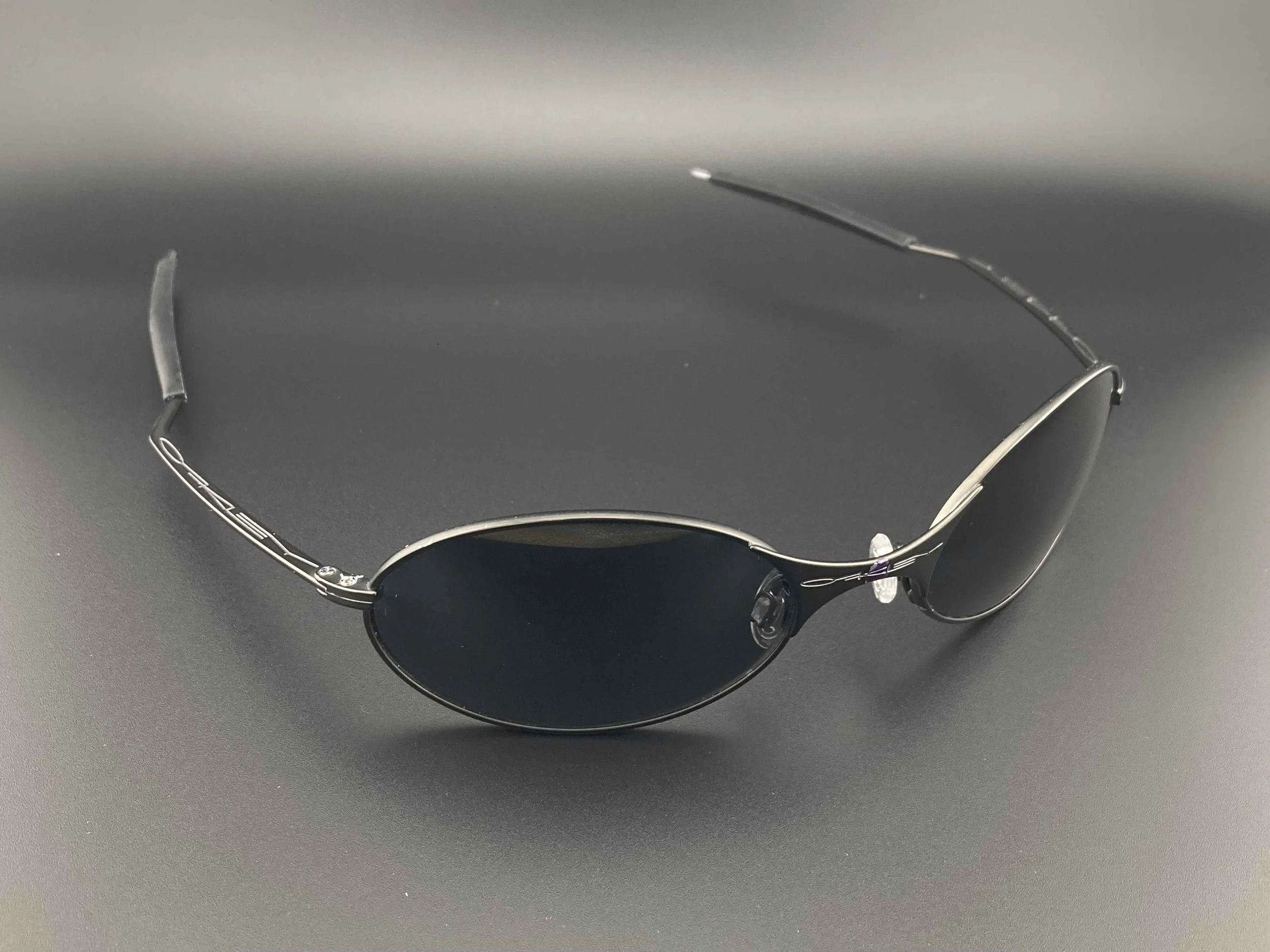 Pair of sleek, black sunglasses with thin metallic frames on a dark surface.