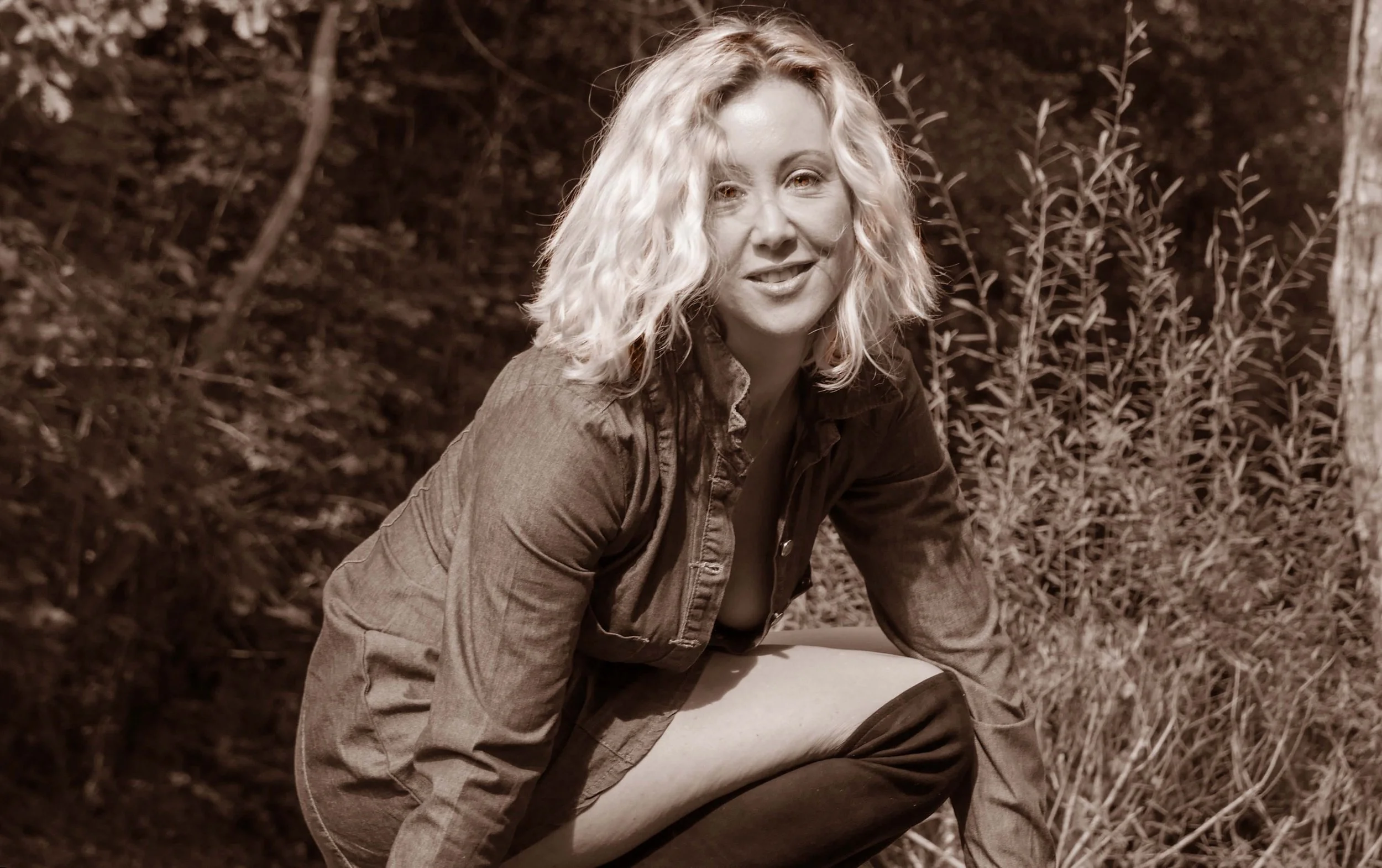 Femme aux cheveux blonds souriant dans un cadre naturel.