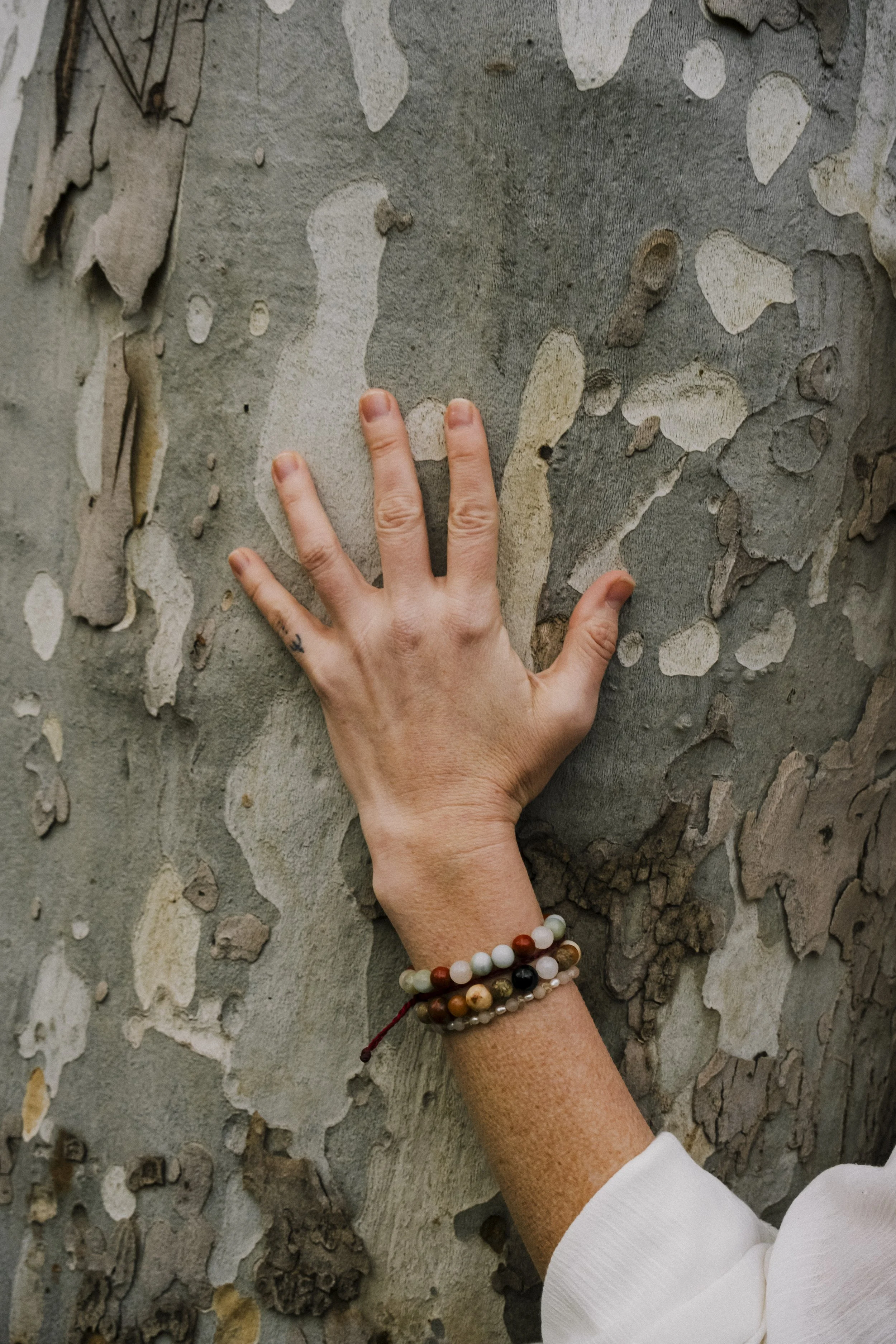 A person's hand with a beaded bracelet touching a textured, peeling wall.