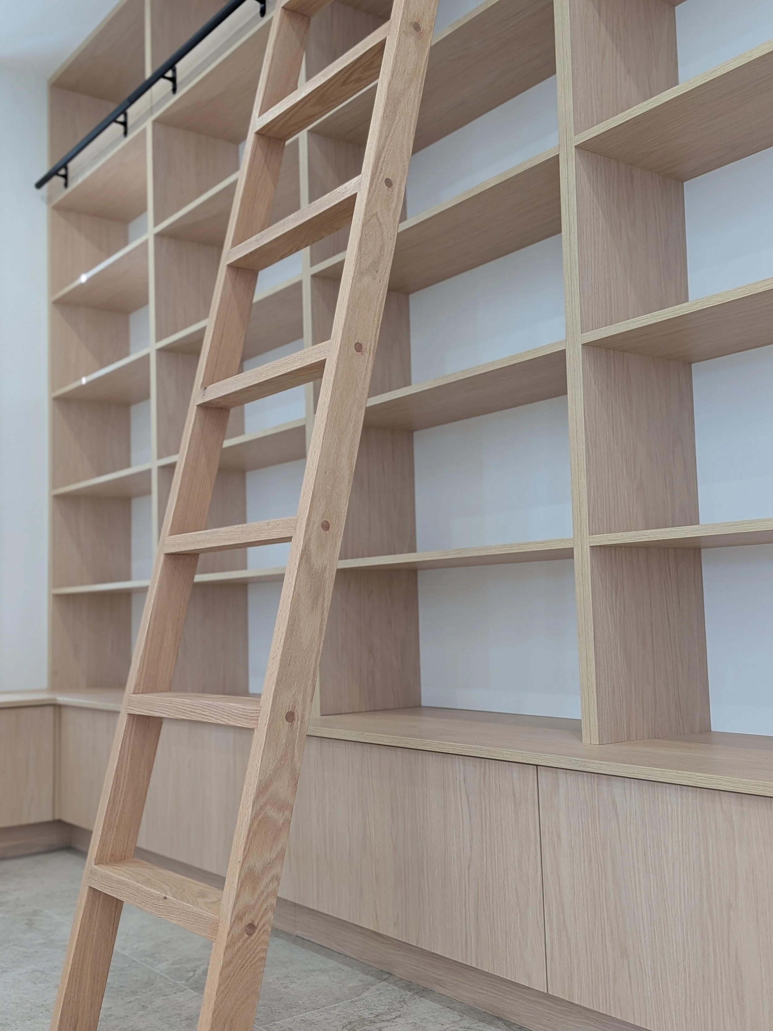 Wooden ladder leaning against large wooden shelving unit with empty cubbies.