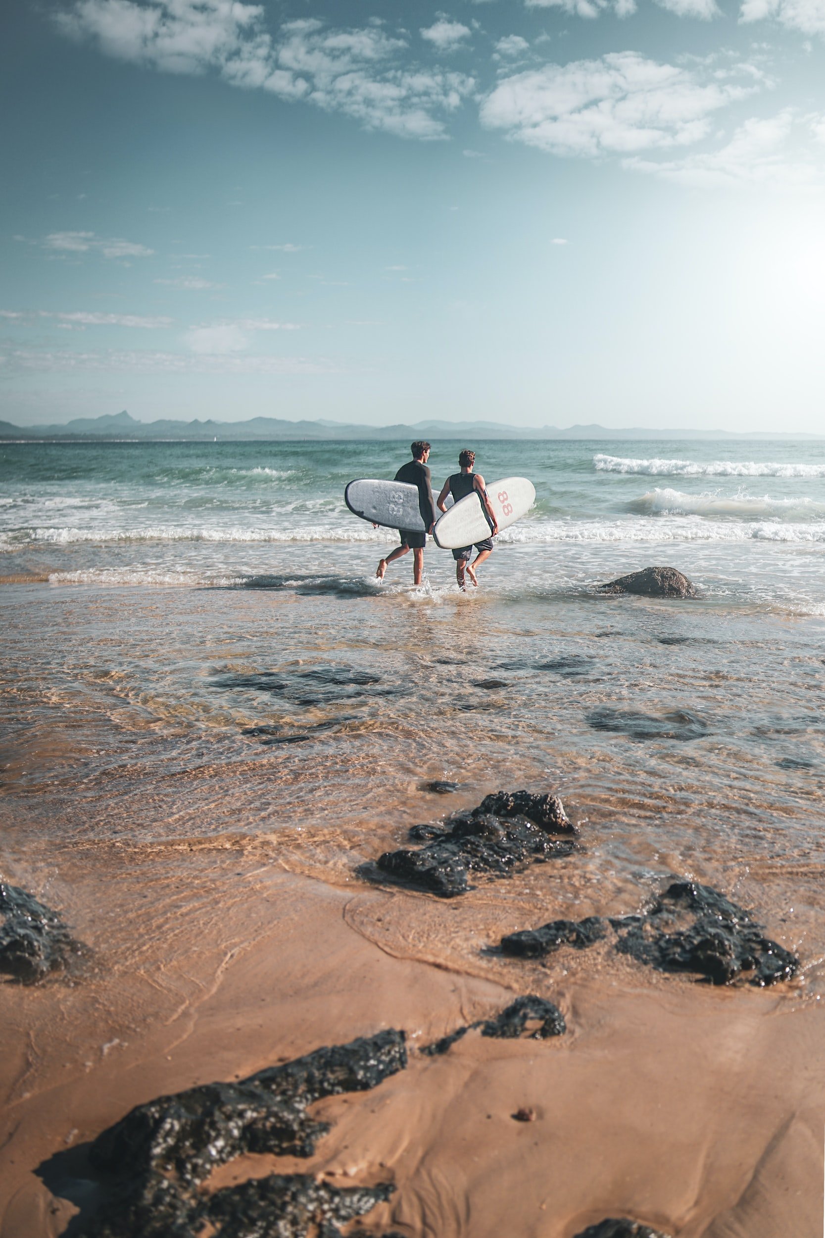 2 surfers walking with surfboards at the Pass beach Byron Bay