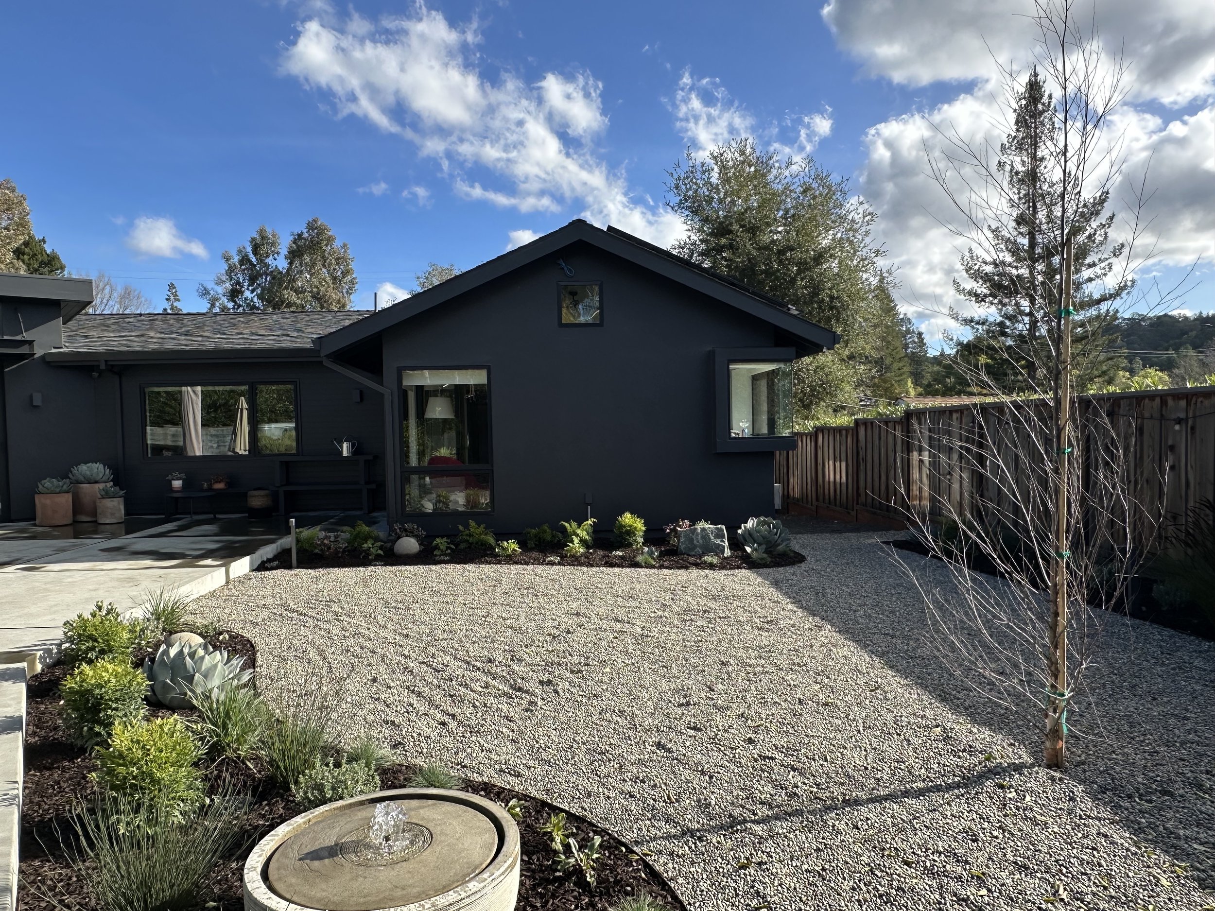 A modern drought-tolerant back yard landscape design featuring a gravel garden, native plants, and sculptural succulents in front of a contemporary dark-painted home