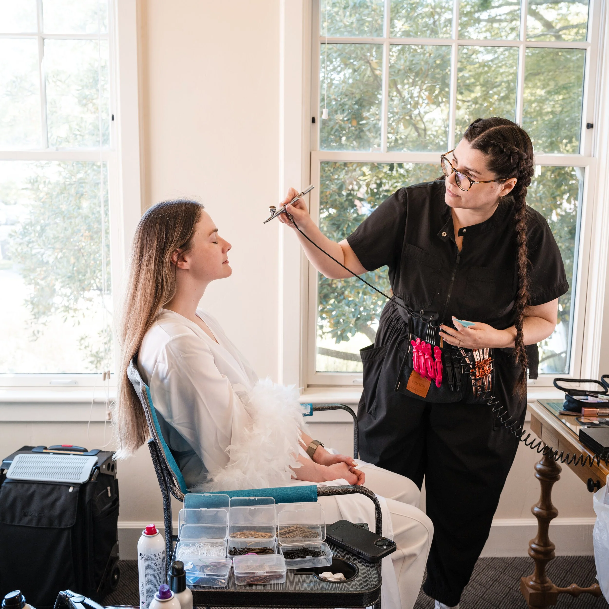 Professional bridal makeup artist, applying airbrush makeup to bride during wedding morning, hair and makeup preparation. A bridal makeup artist applying airbrush makeup during the bride's wedding morning beauty preparation. Airbrush makeup the perfo