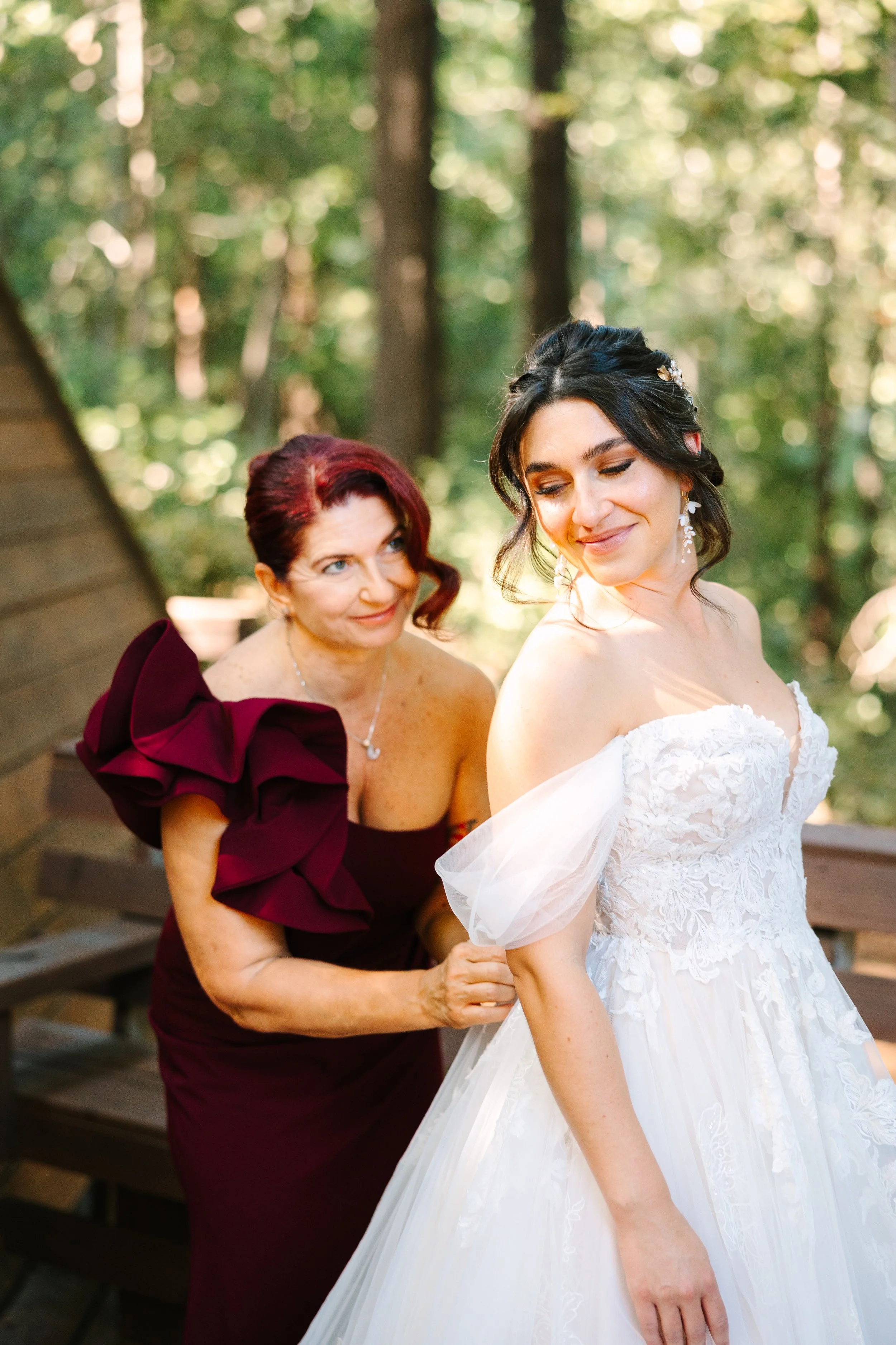 Bride getting into wedding dress during redwood forest wedding with soft natural bridal makeup and romantic updo by Beauty by Santi. BRIDE being helped by mom mother of the bride helping Bride get ready. Mother of the bride chic classy French twist u