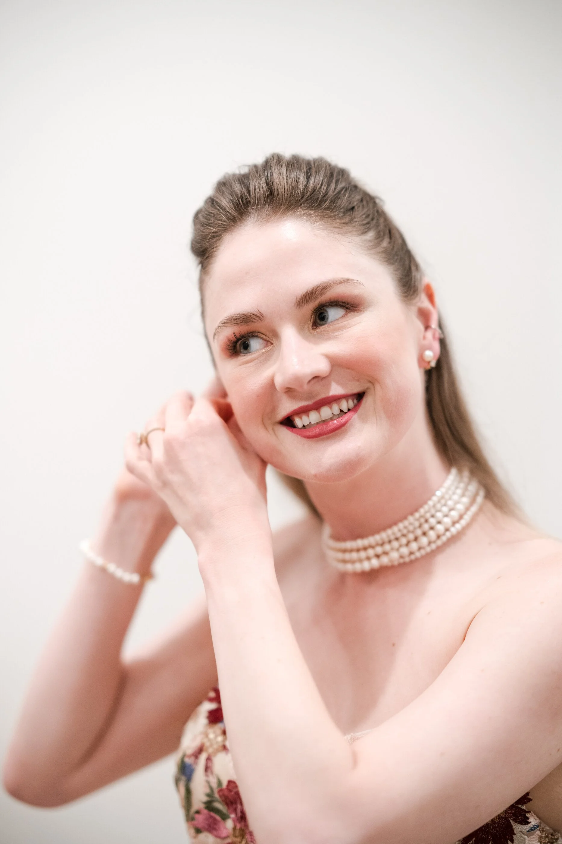 Bride smiling while adjusting her earrings showing natural wedding makeup and soft, half a bridal hairstyle natural bridal hair and make up look bride, finishing her look with soft romantic bridal hair and natural wedding makeup a bride, smiling as s