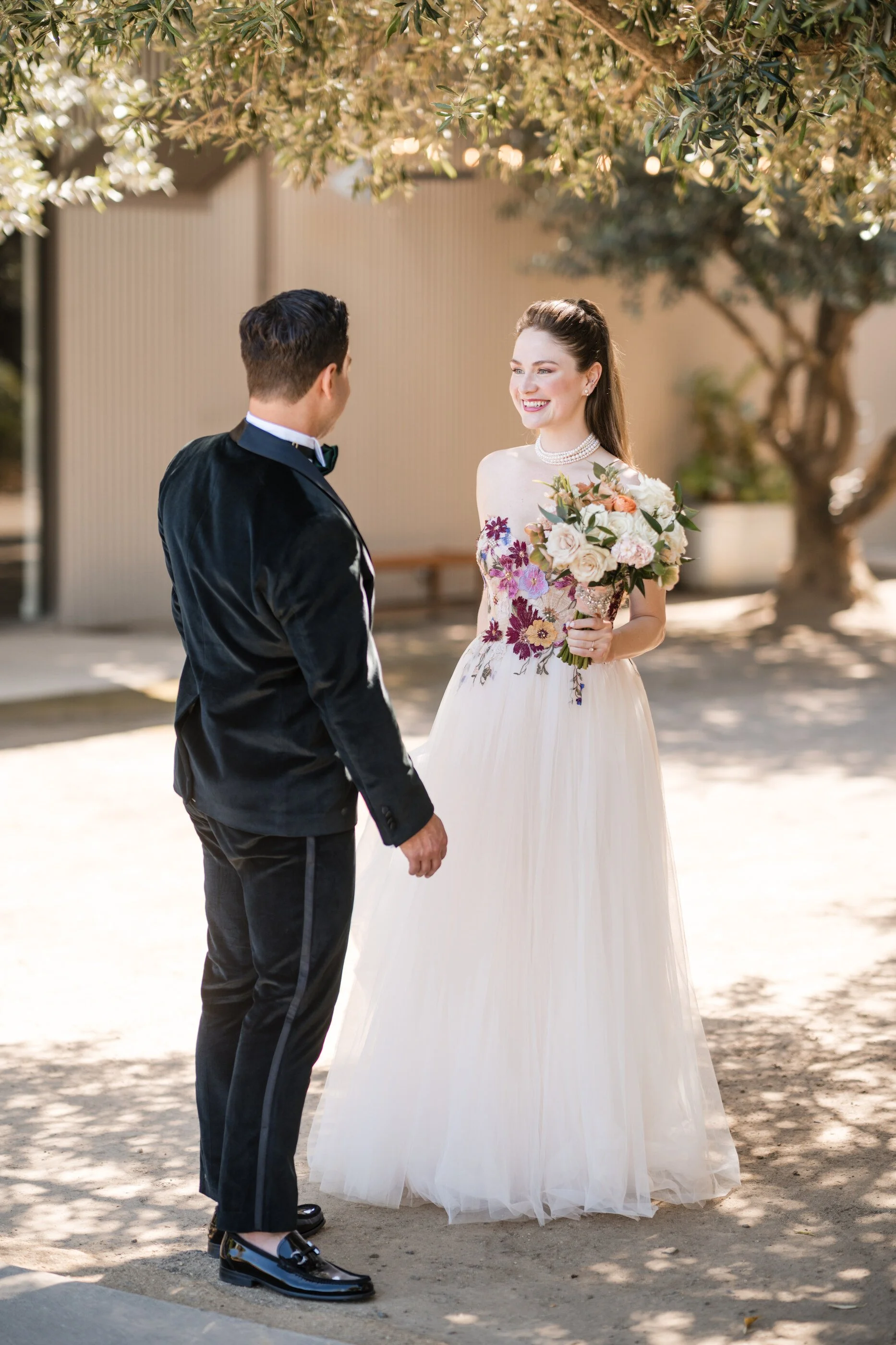 Bride and groom, first look in romantic garden, setting with bride, holding peach and ivory bouquet and wearing embroidered floral wedding gown