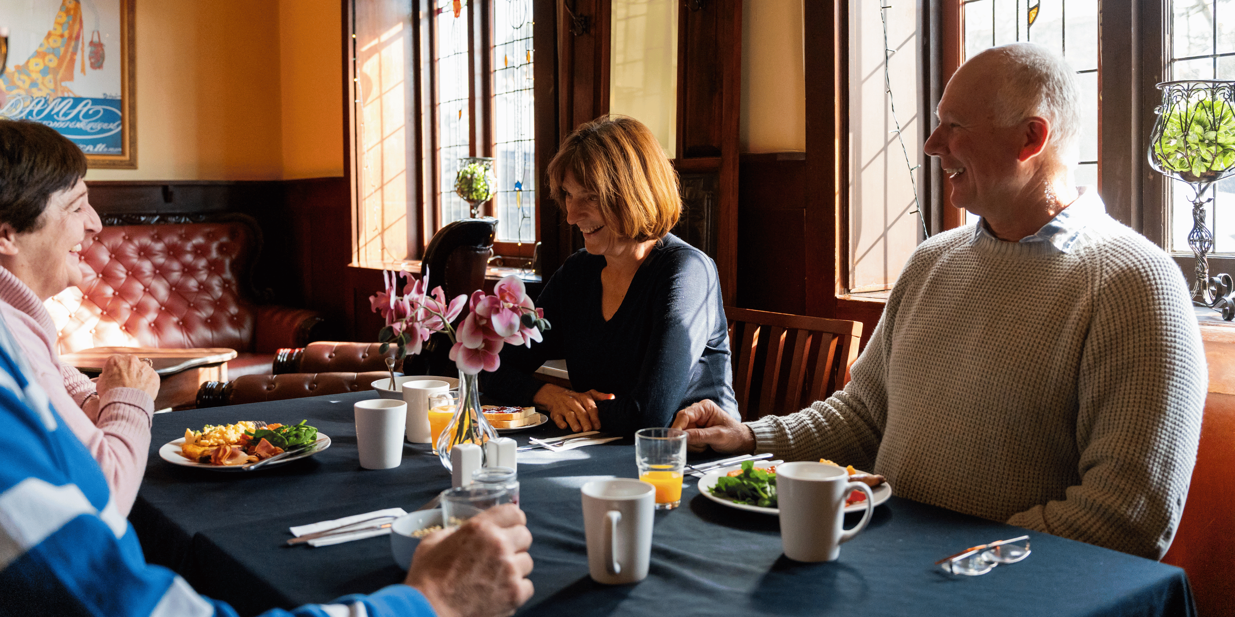 Four people sitting around a table in a dining room, smiling and engaging in conversation, with plates of food and drinks in front of them.