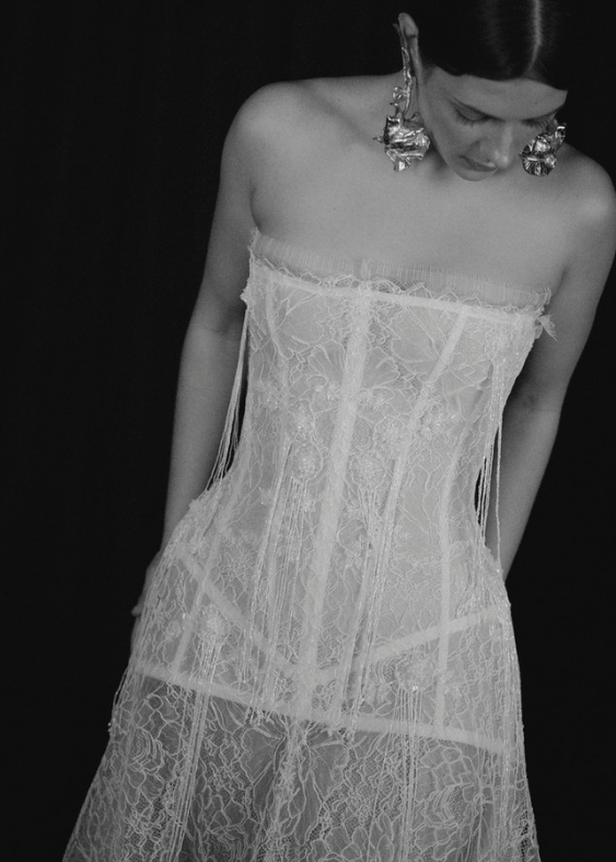 Picture of a modern Australian bride looking down with large earrings and a detailed, delicate lace gown with a boned corset.