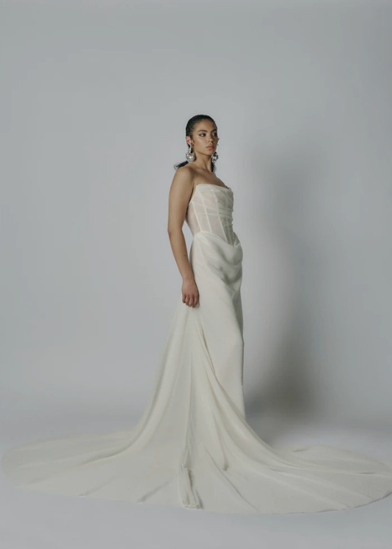 Picture of a contemporary, fashionable Australian Bride wearing a sheer, corseted, wedding gown on a neutral background facing to the side.