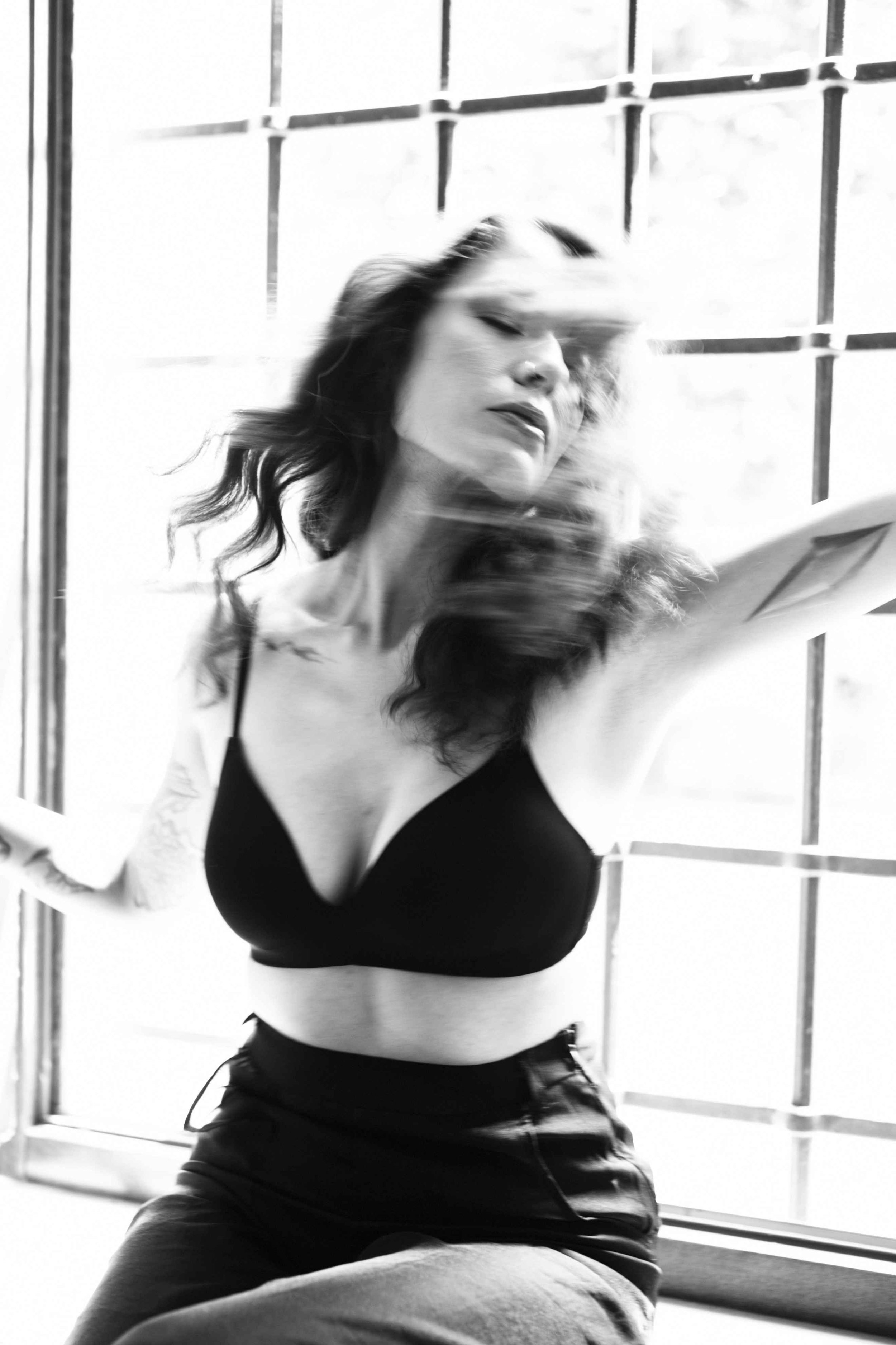 Black and white image of a woman wearing a black top, sitting by a window, with motion blur.
