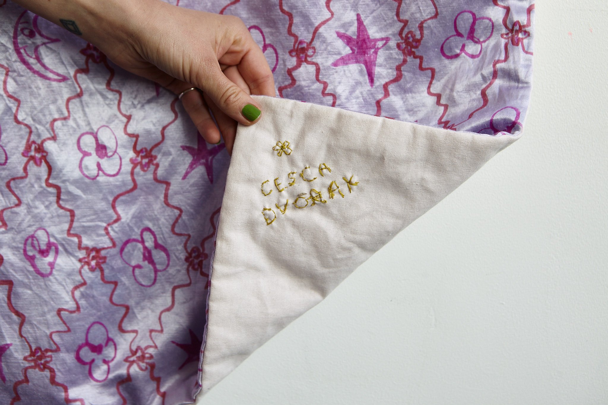 Photograph of Cesca Dvorak hand revealing embroidered name on corner of silk quilt