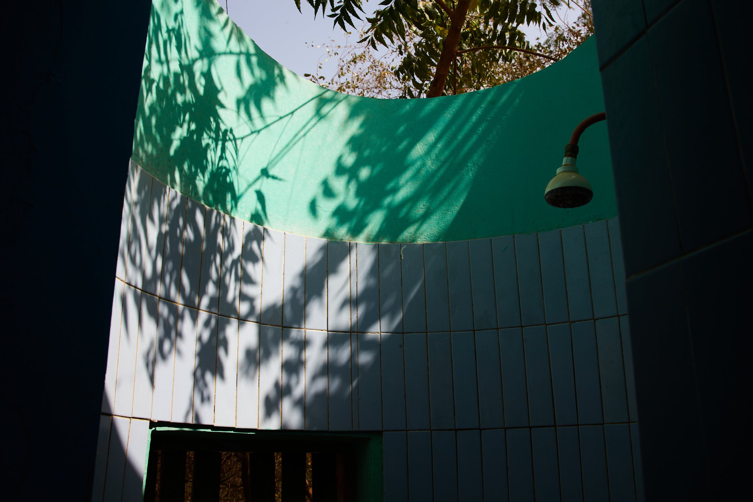 Photograph of shadows of trees on green and blue tiled wall inside an outside shower at Ecoles Des Sables taken by photographer Hatty Frances Bell