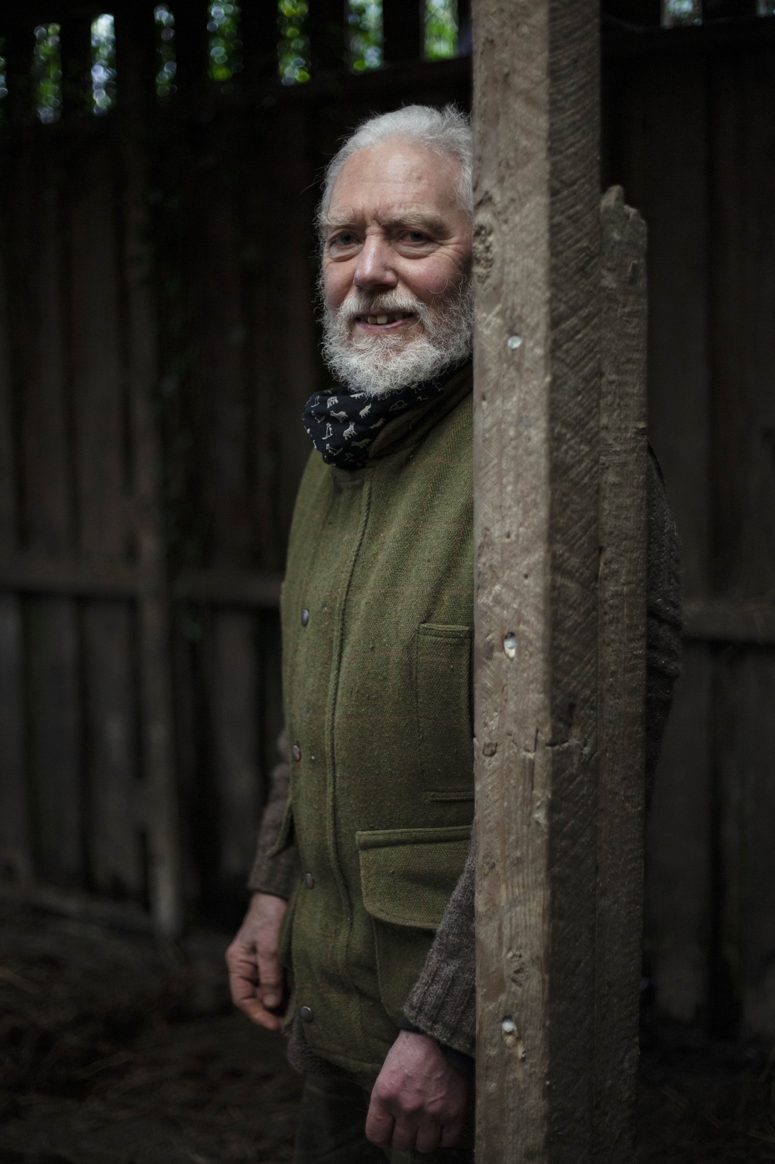 A portrait photograph by Hatty Frances Bell of sheep farmer standing in his barn leaning against post 