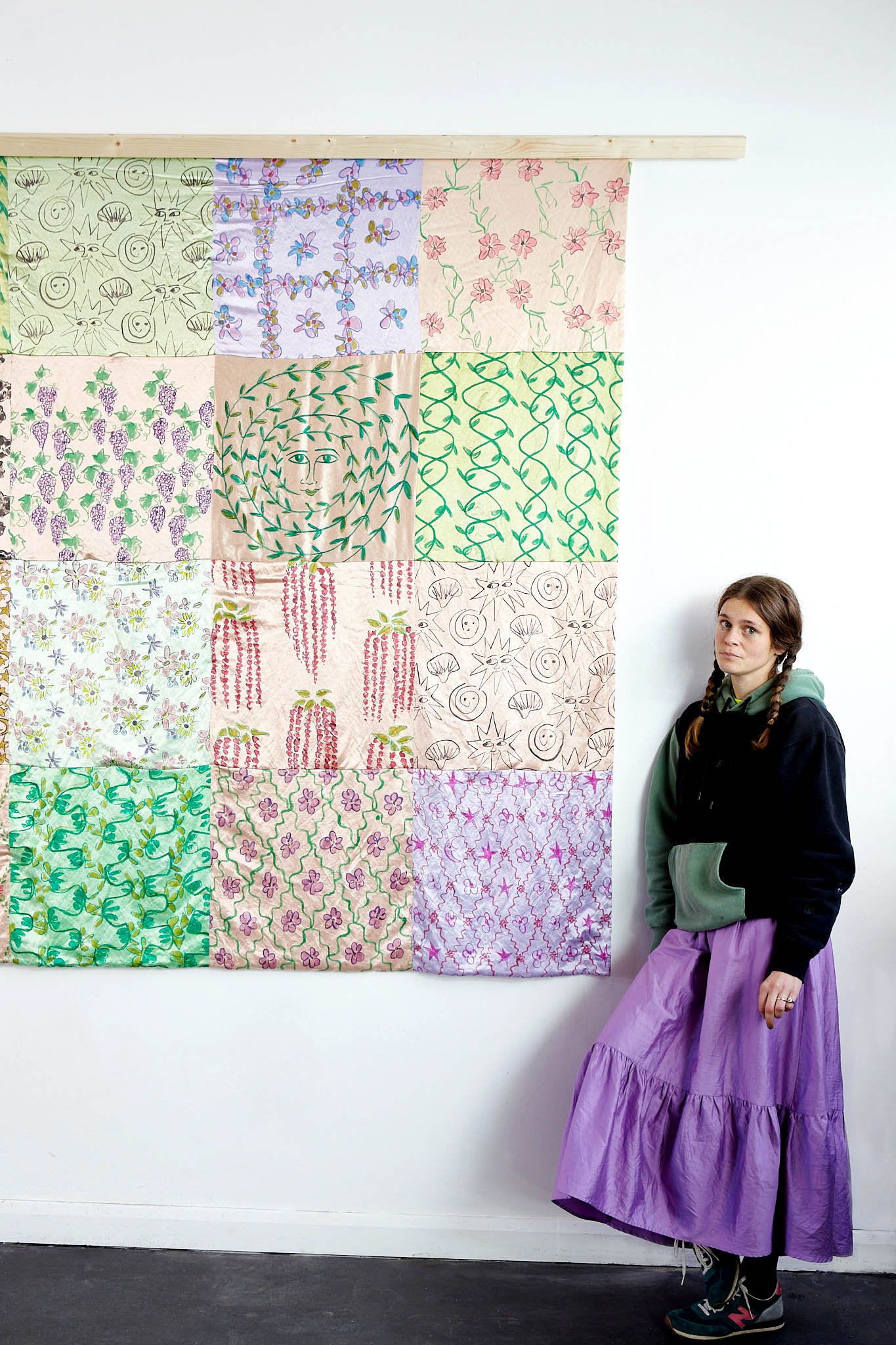 Cesca Dvorak stands next to her silk patchwork quilt hanging on a white wall in Stroud