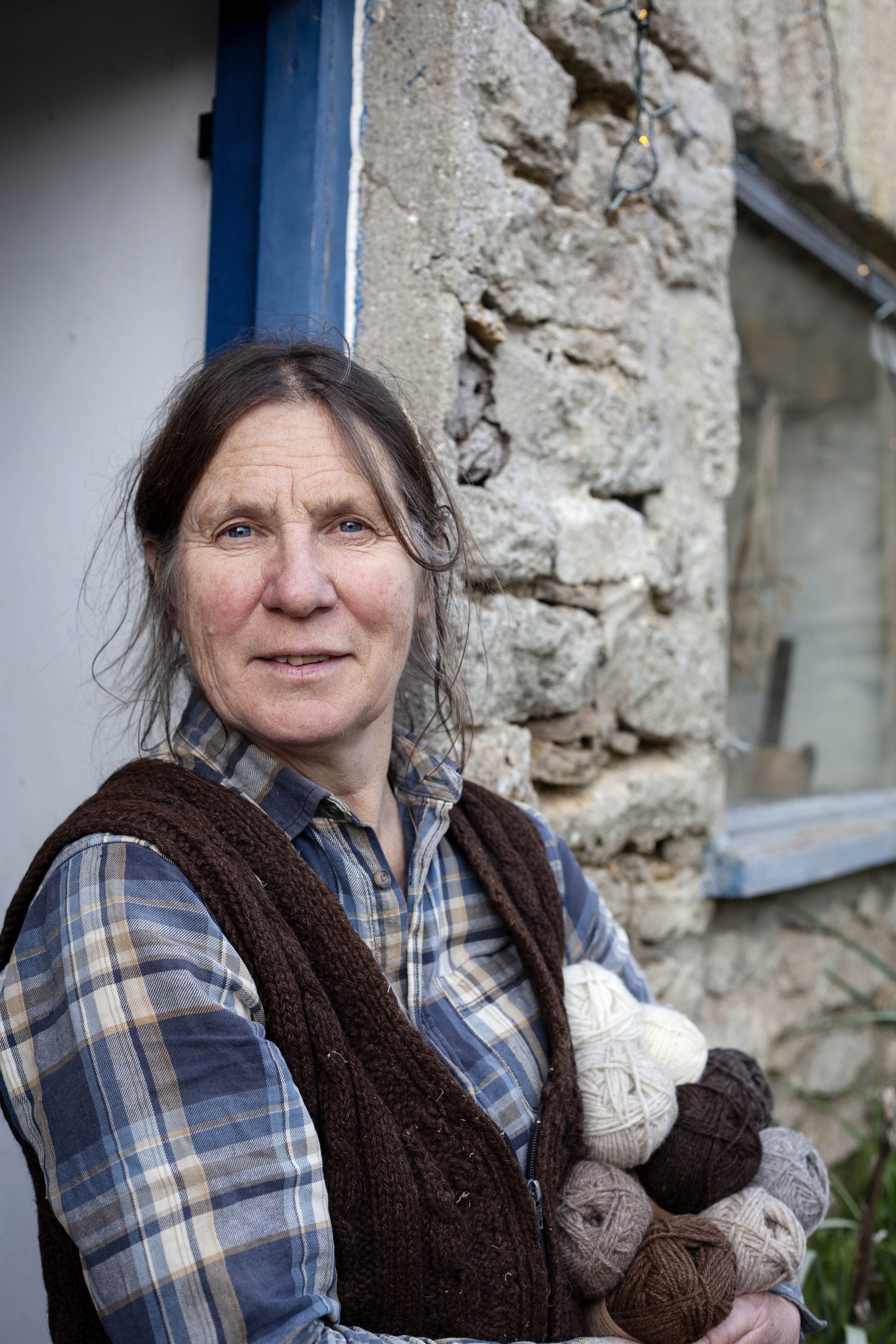Portrait photograph of Ellen at Tamerisk Farm standing in blue doorway holding balls of wool