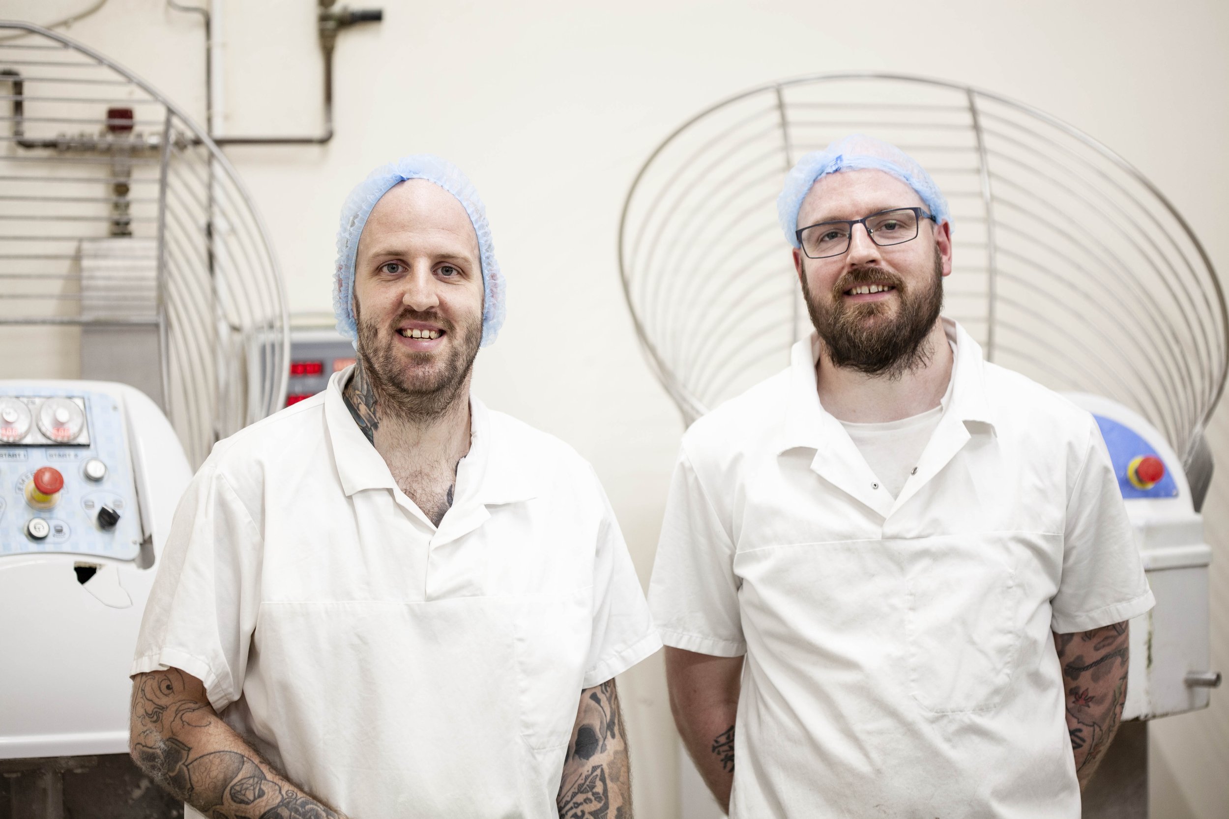 Landscape photograph by Hatty Frances Bell of two male bakers at Linzers Bakery in Norwich wearing white clothing and blue hairnets