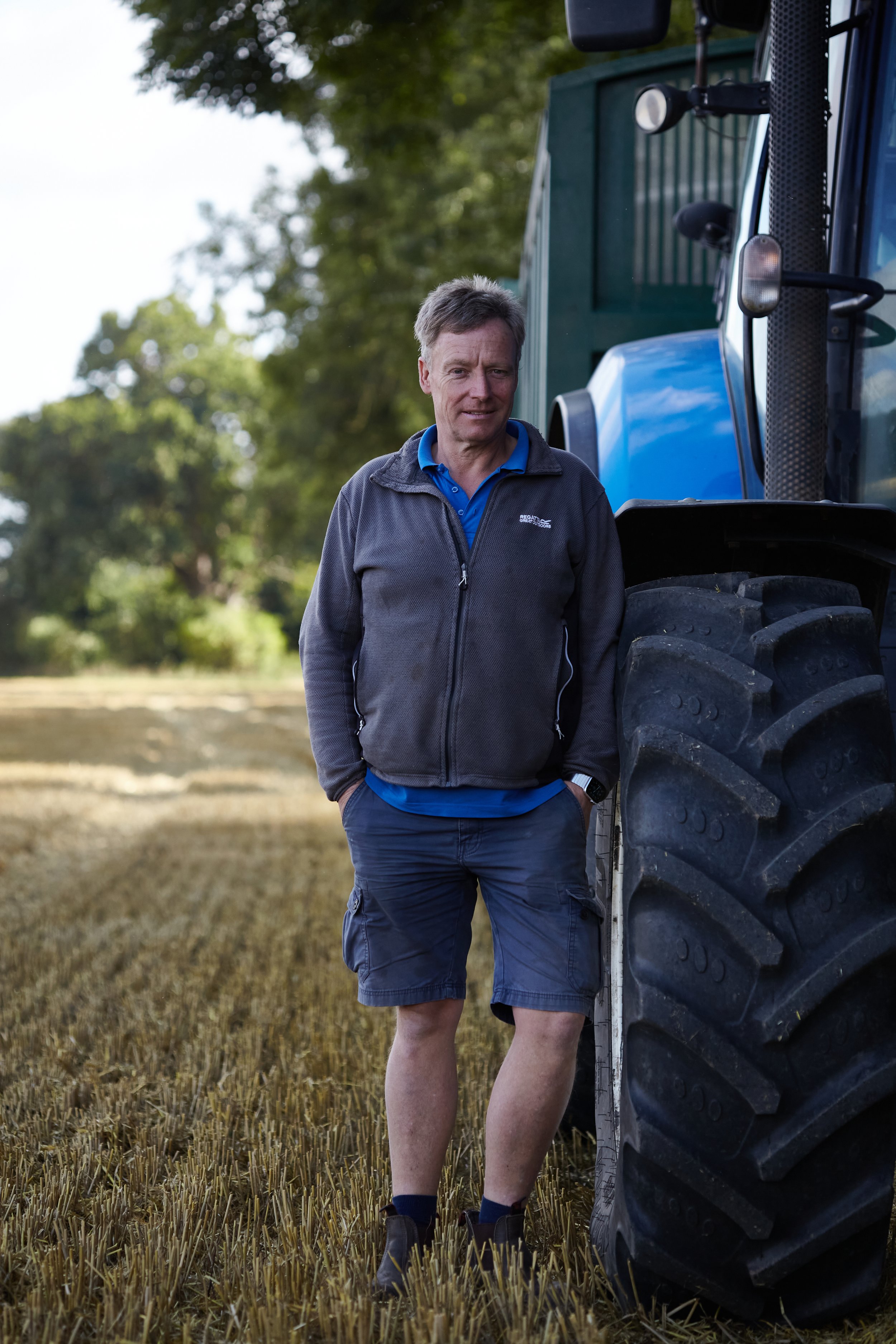 Portrait photograph of man standing next to blue tractor in field in Norfolk