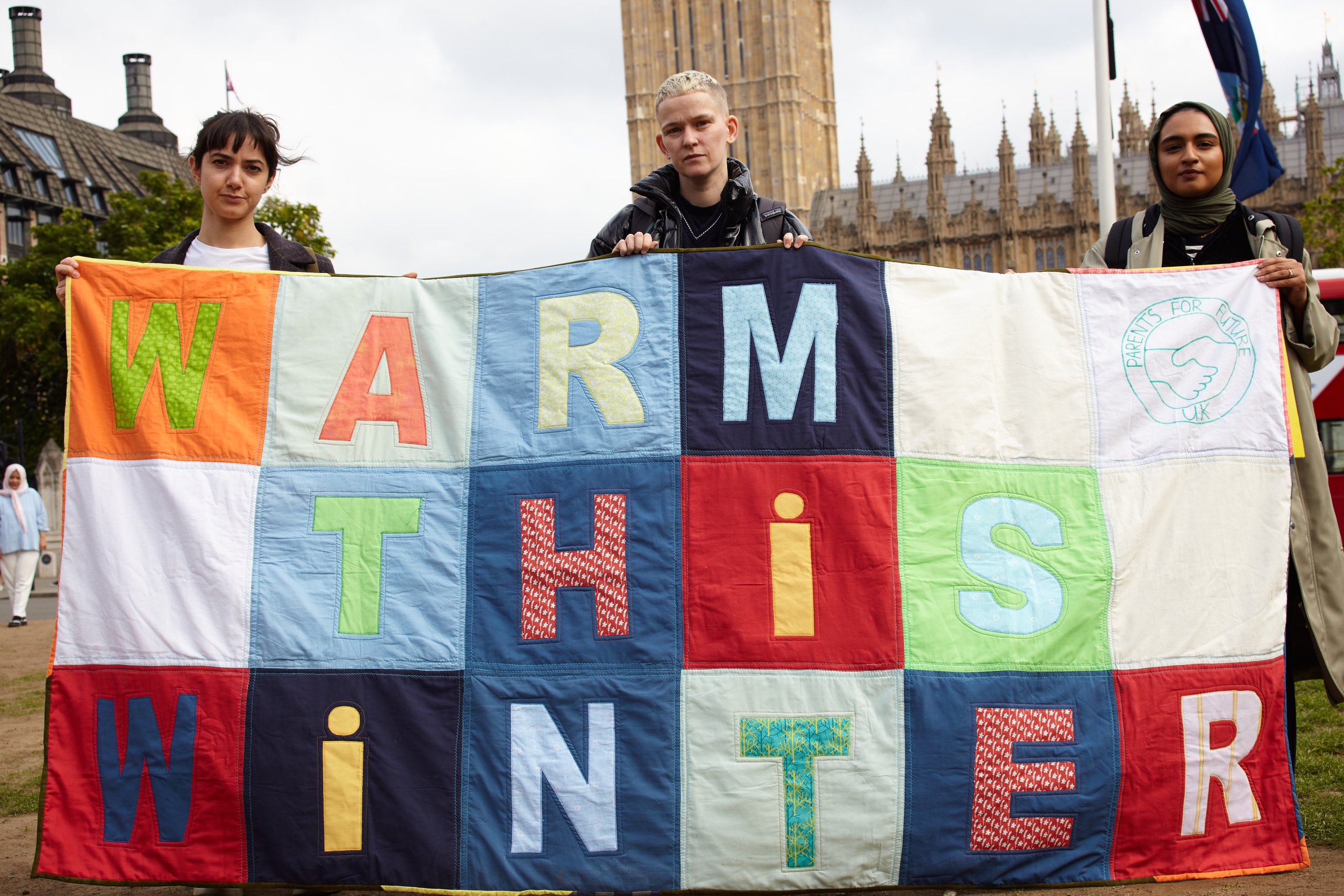 Photograph by Hatty Frances Bell of three women holding Warm This Winter placard at political demonstration in London 