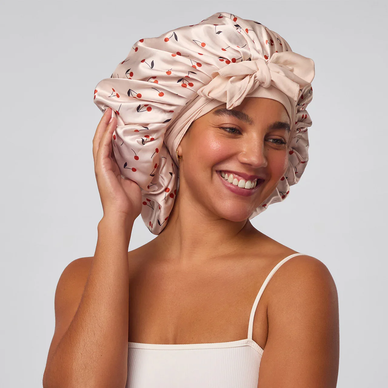 Woman wearing a satin bonnet with cherry print — protective hair accessory for preserving curls overnight.