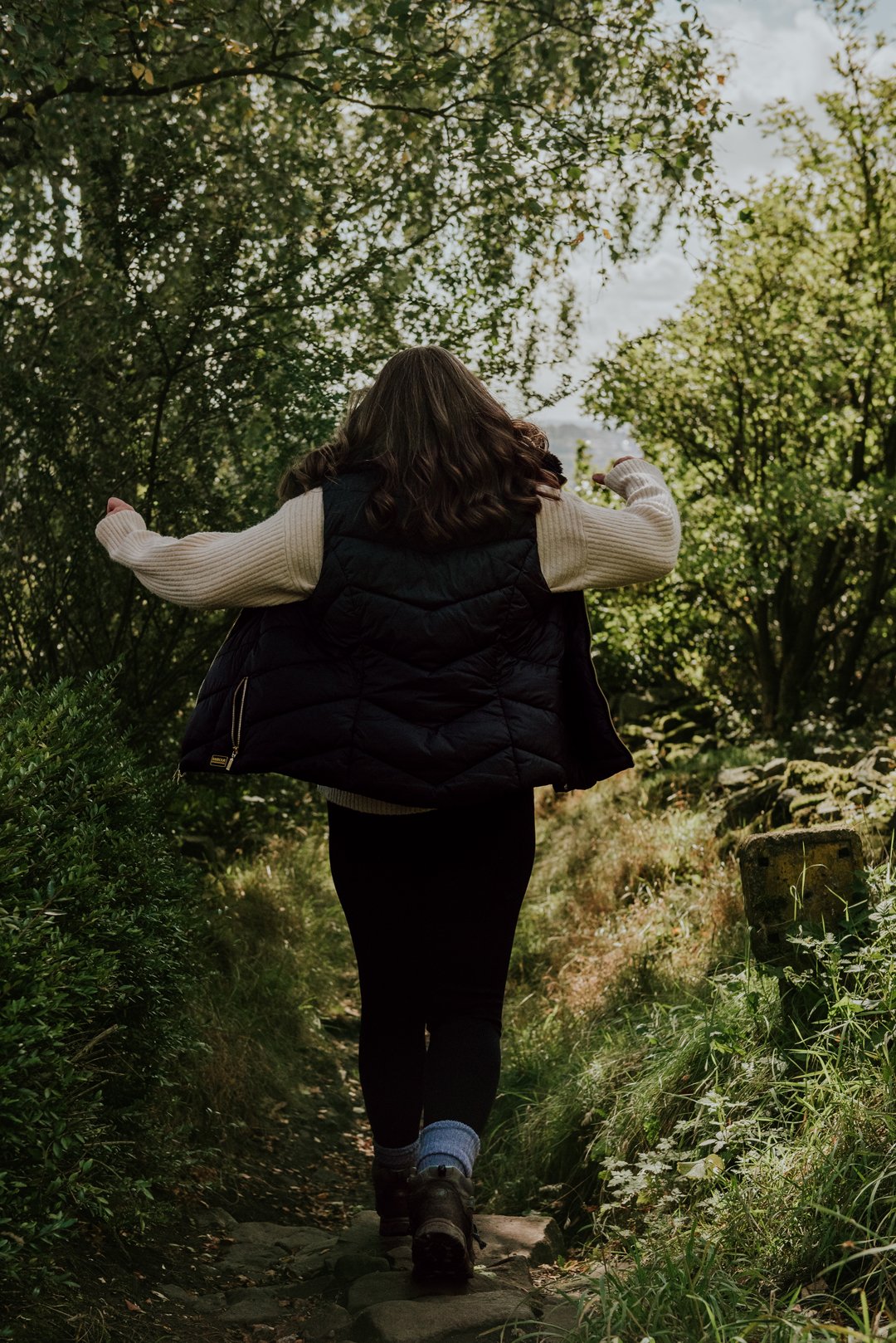 Jen, The Therapy Nook. Jen is walking through the woods, she is happy and jumping as she walks away from the camera.