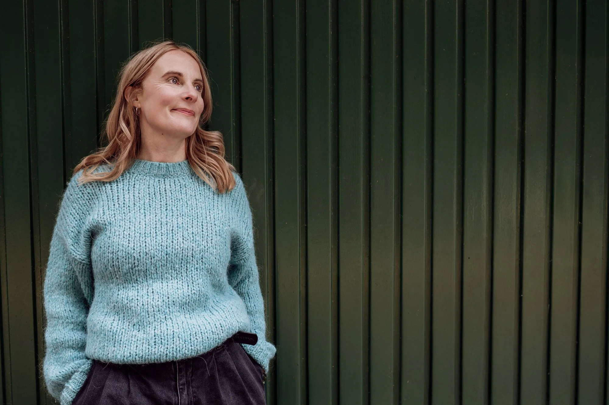 Sophie Longden Therapy. Sophie is dressed in blue and standing in front of a green panelled wall.