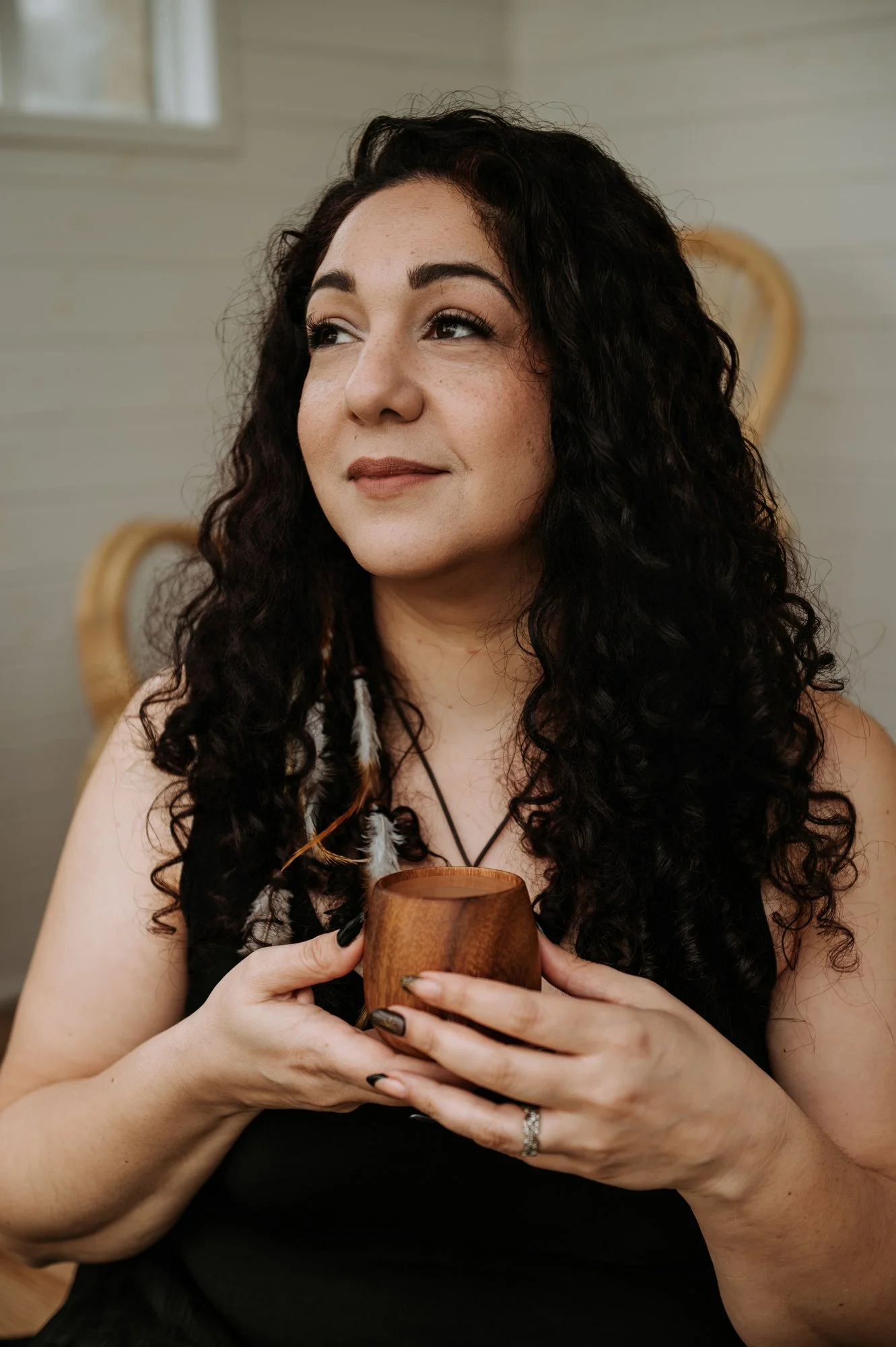 El Jedras, woman dressed in black, she is looking to the side with a gentle smile. She is holding a wooden cup full of sacred cacao.