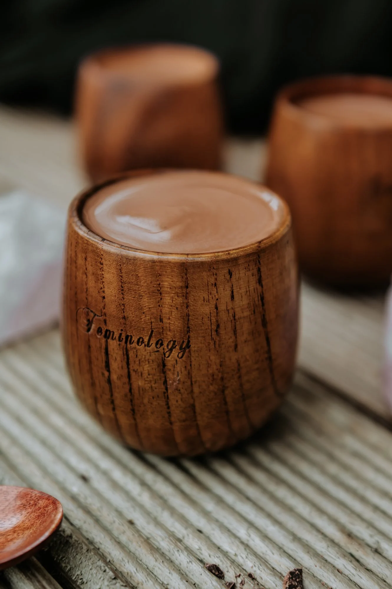 A wooden cup filled to the top with thick creamy sacred Cacao. The cup has 'Feminology' carved into the side. 