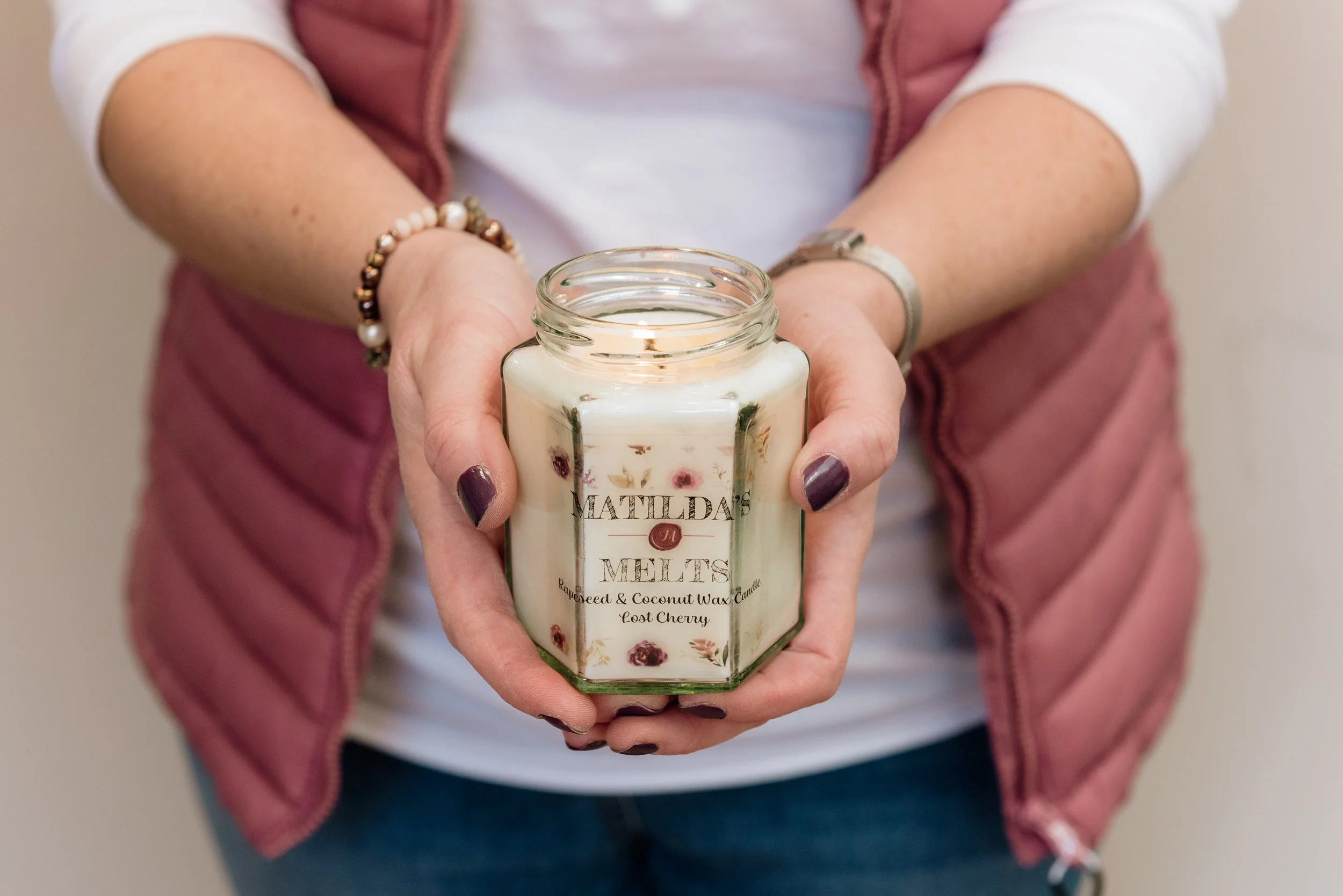 Woman dressed in pink and white holding our her hand poured candles