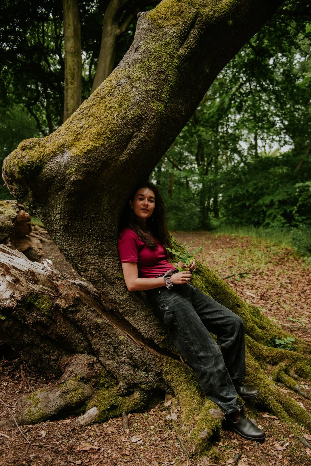 Ellie Belfield, Therapist. She is outdoors and relaxing back into a curved tree truck. 