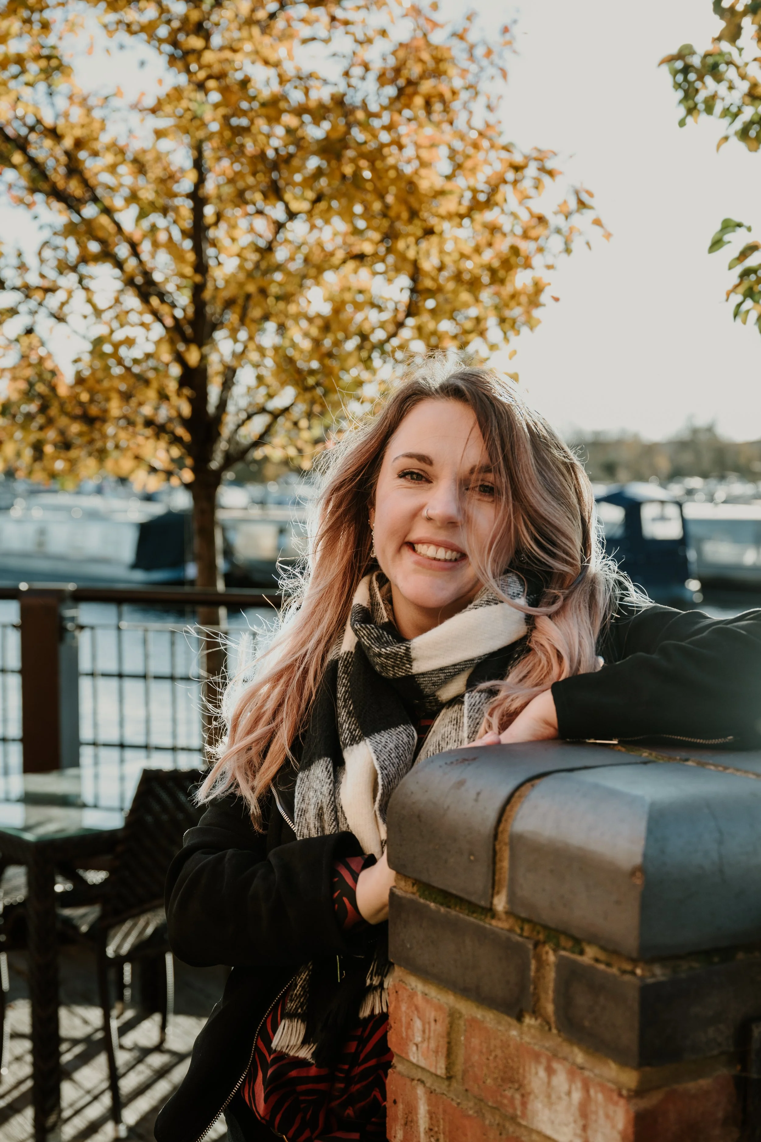 Sarah smiling into the camera, hair blowing around. She is wearing a black and white scarf.