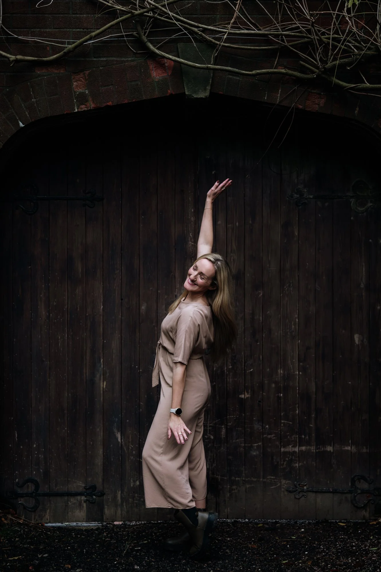April Wild, Wild & Wild events. She is standing in front of a huge wooden gate, with one arm extended up. She is looking very happy.