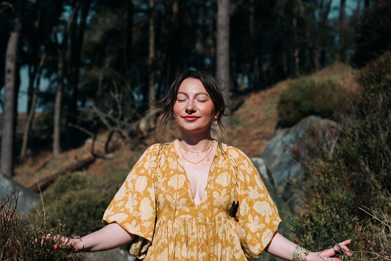 Molly Gould, Effable. She is dressed in a yellow dress standing in the middle of a path. The sun is lighting her up, her eye are closed and she is smiling.