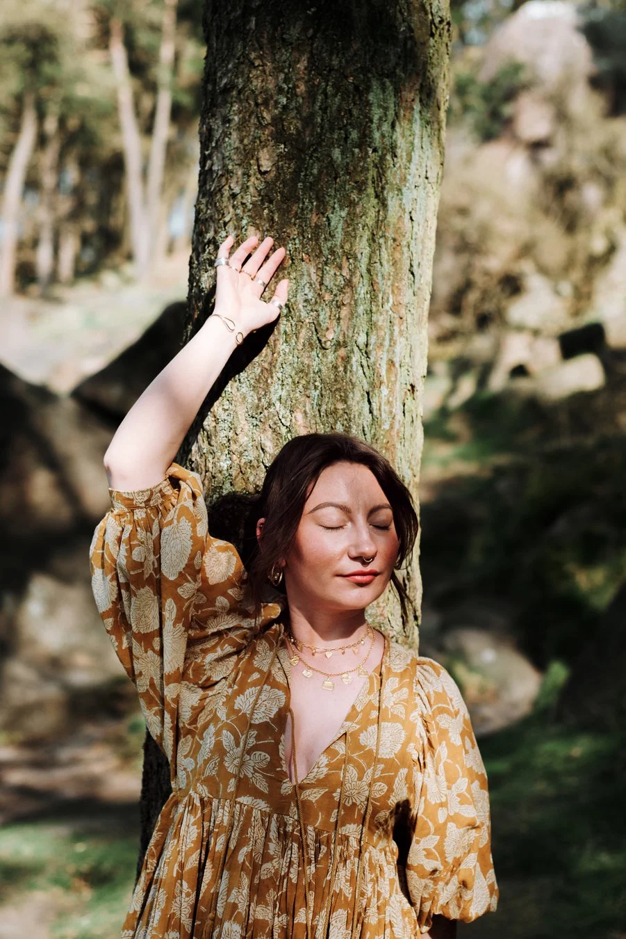 Molly Gould, Effable. Molly is dressed in yellow and is leaning up against a tree, one arm reaching up.