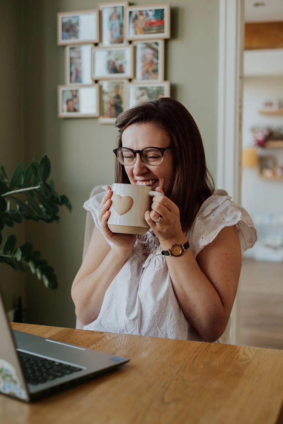 Little Green Gem Marketing. Gem is holding up her mug in front of her while she laughs. She is sitting at her desk with her laptop open. 