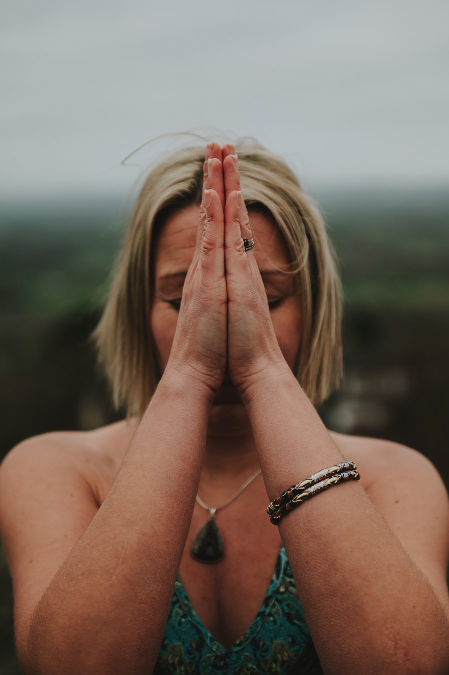 Kundalini with Kelly. Woman with blonde hair, her hands are in front of her face in prayer position.