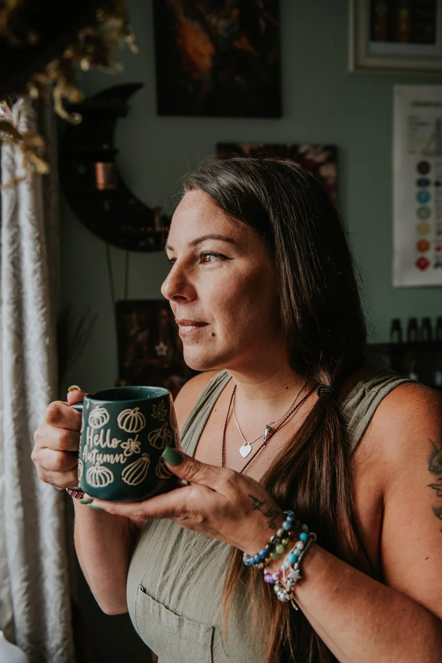 Abi, Alternative Advocacy is holding her favourite green Autumnal mug, she is looking out of the window with a gentle smile.