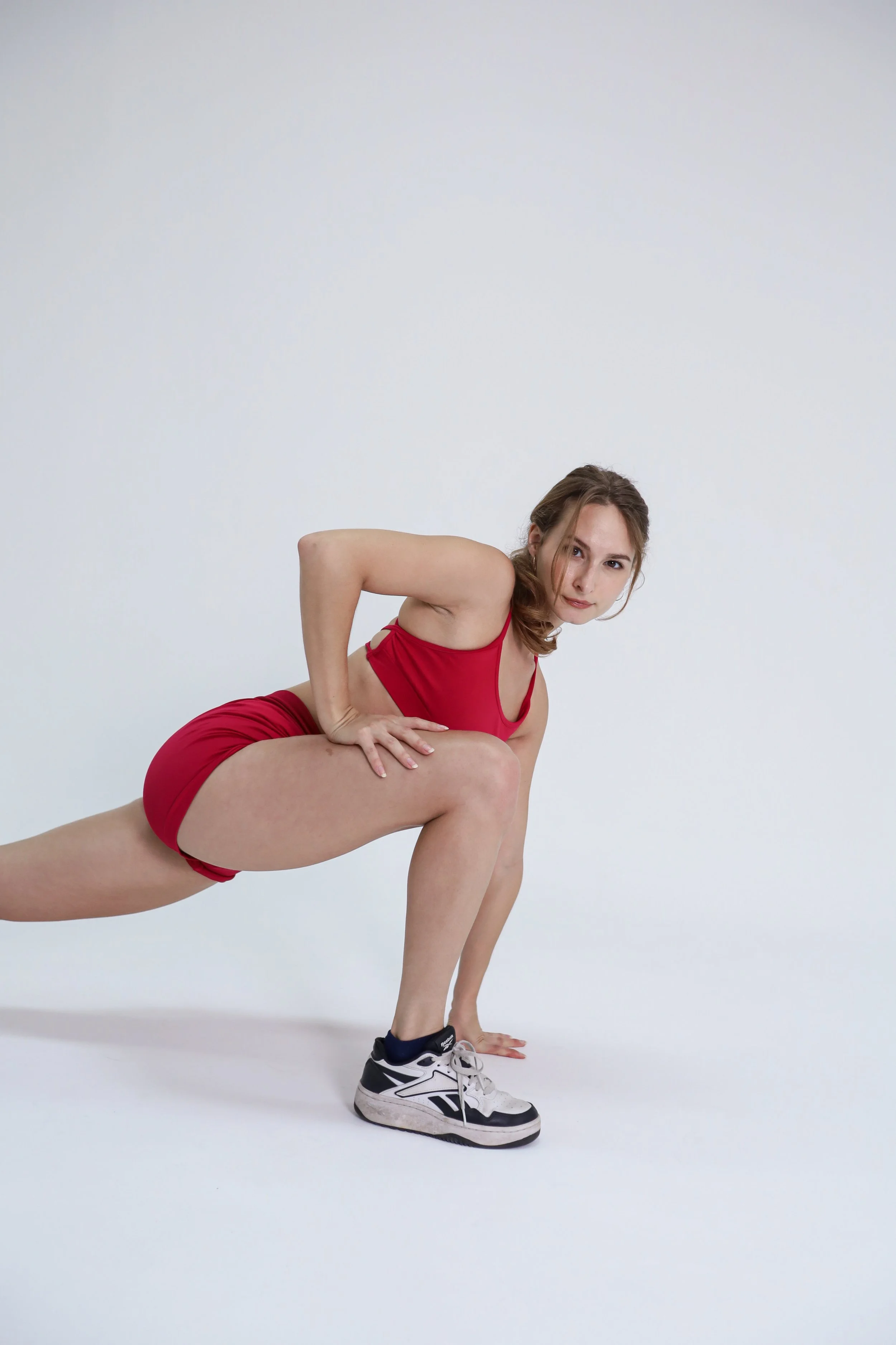 Young woman in red sportswear performing a plank exercise on a white floor against a white background.