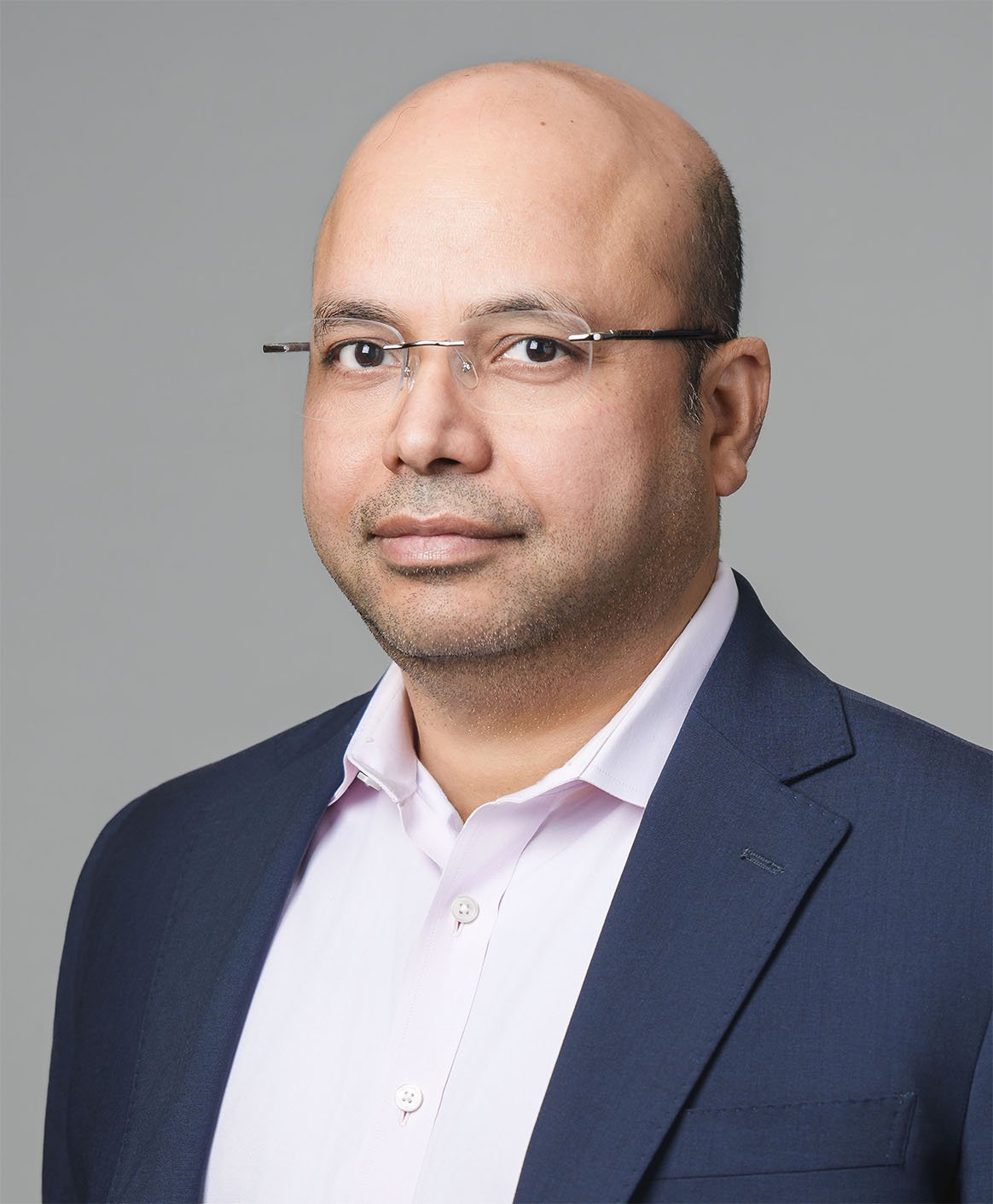 Bijendra Vishal
Principal Headshot of a man with glasses, a mustache, and a goatee, wearing a dark suit and a light pink shirt, against a plain gray background.