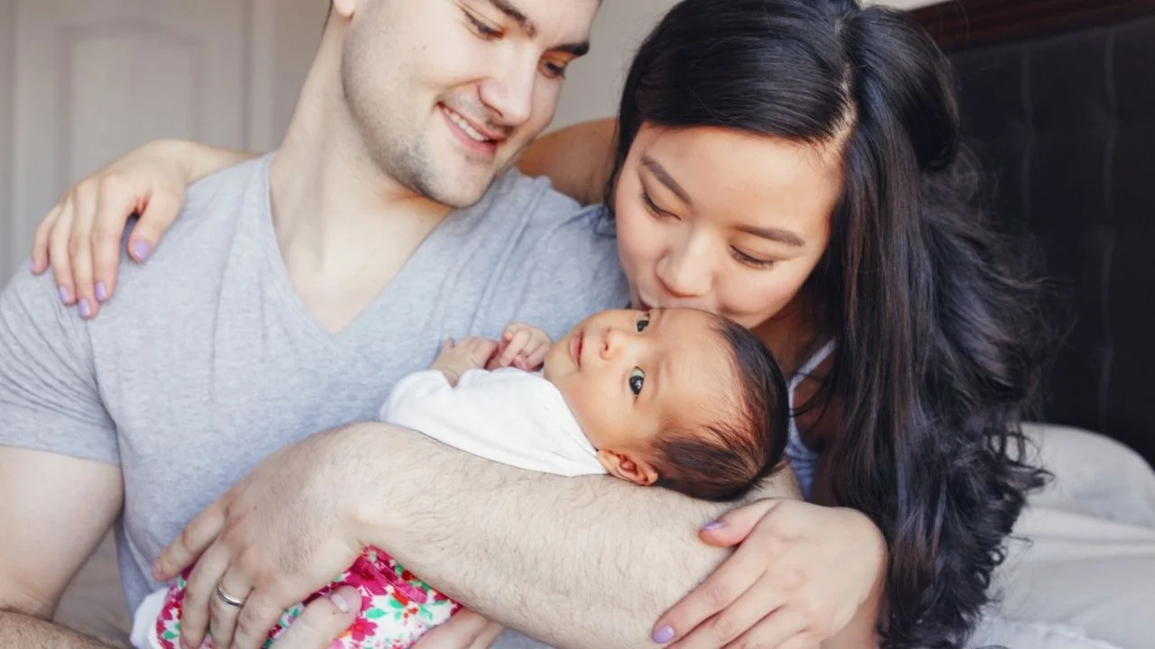 father holding a newborn baby while mother kisses it's head