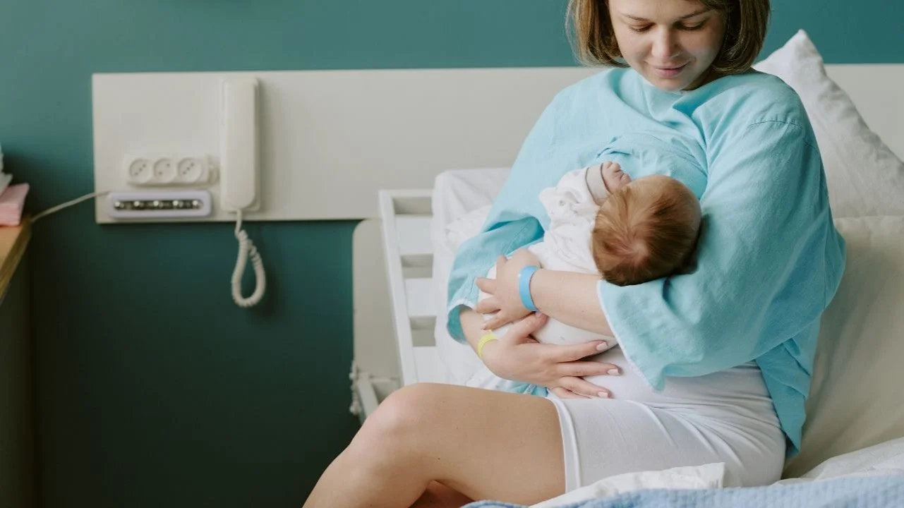 postpartum mom breastfeeding newborn in hospital bed
