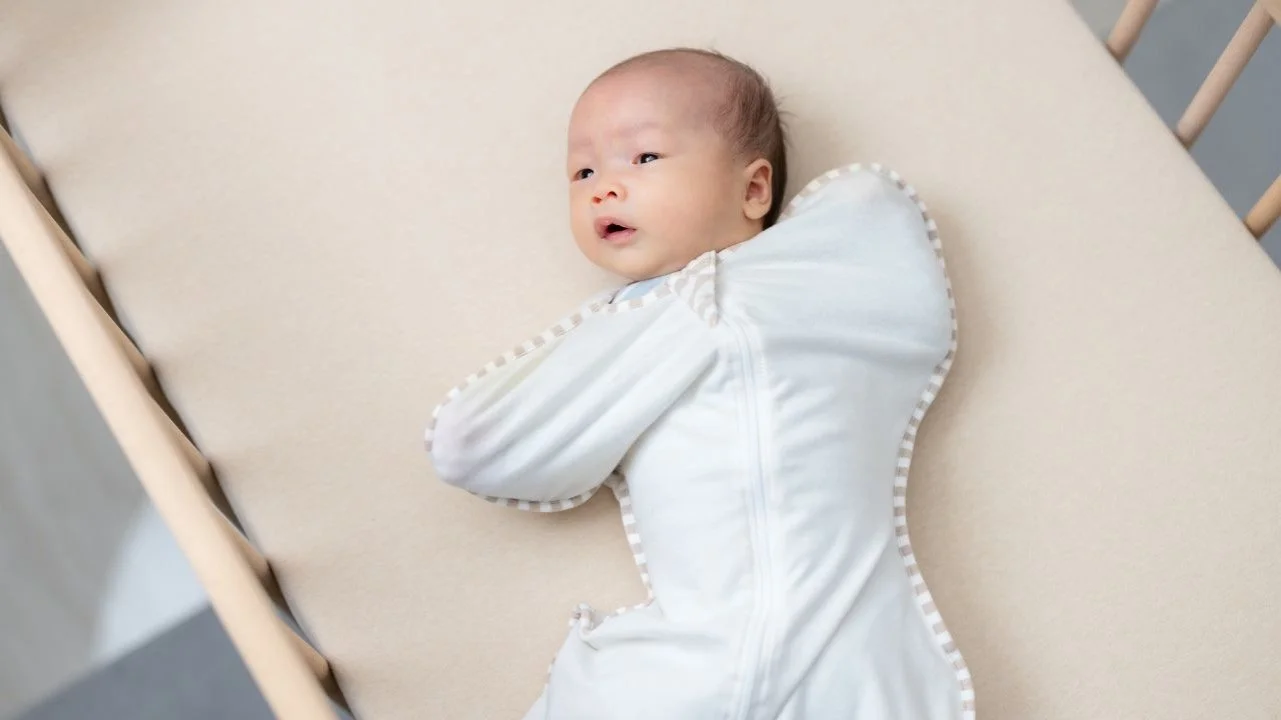 newborn awake in crib in a sleep sack swaddle