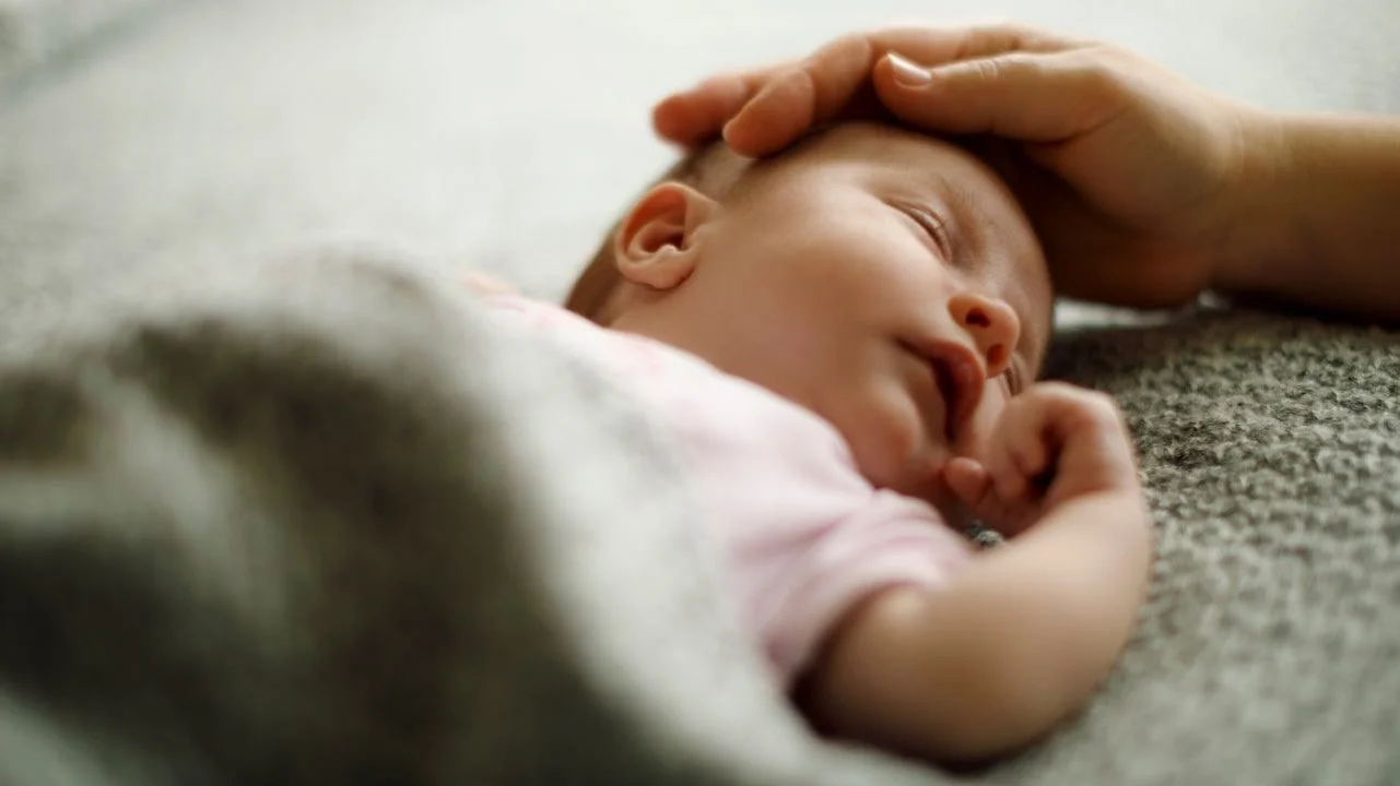 baby sleeping with adult hand cradling its head