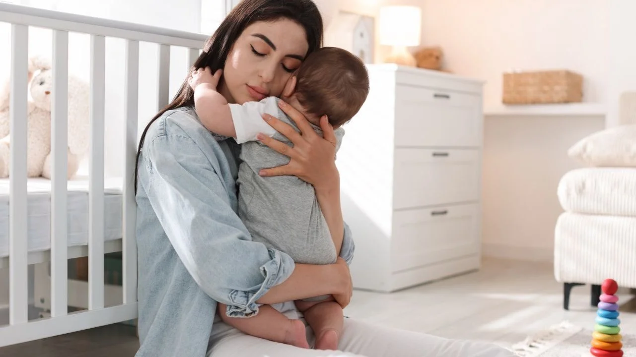 mom sitting on floor of nursery holding baby