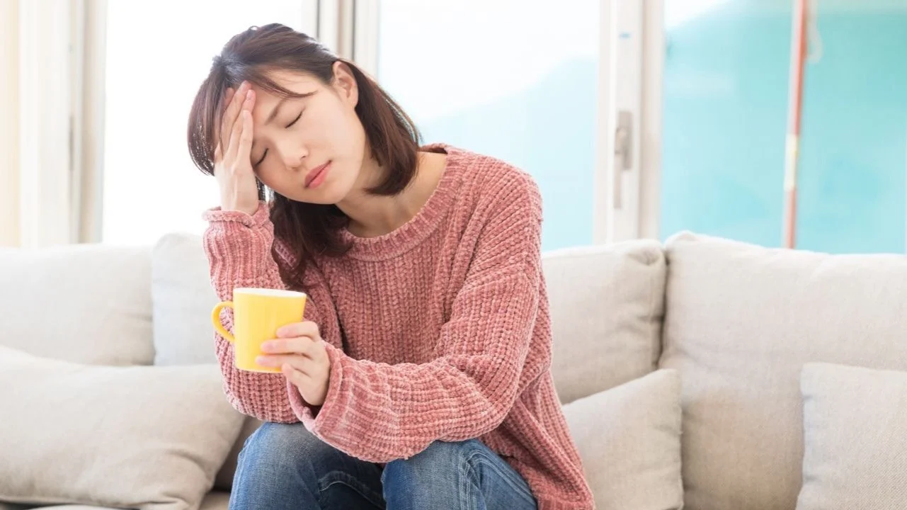 tired woman sitting on couch drinking coffee