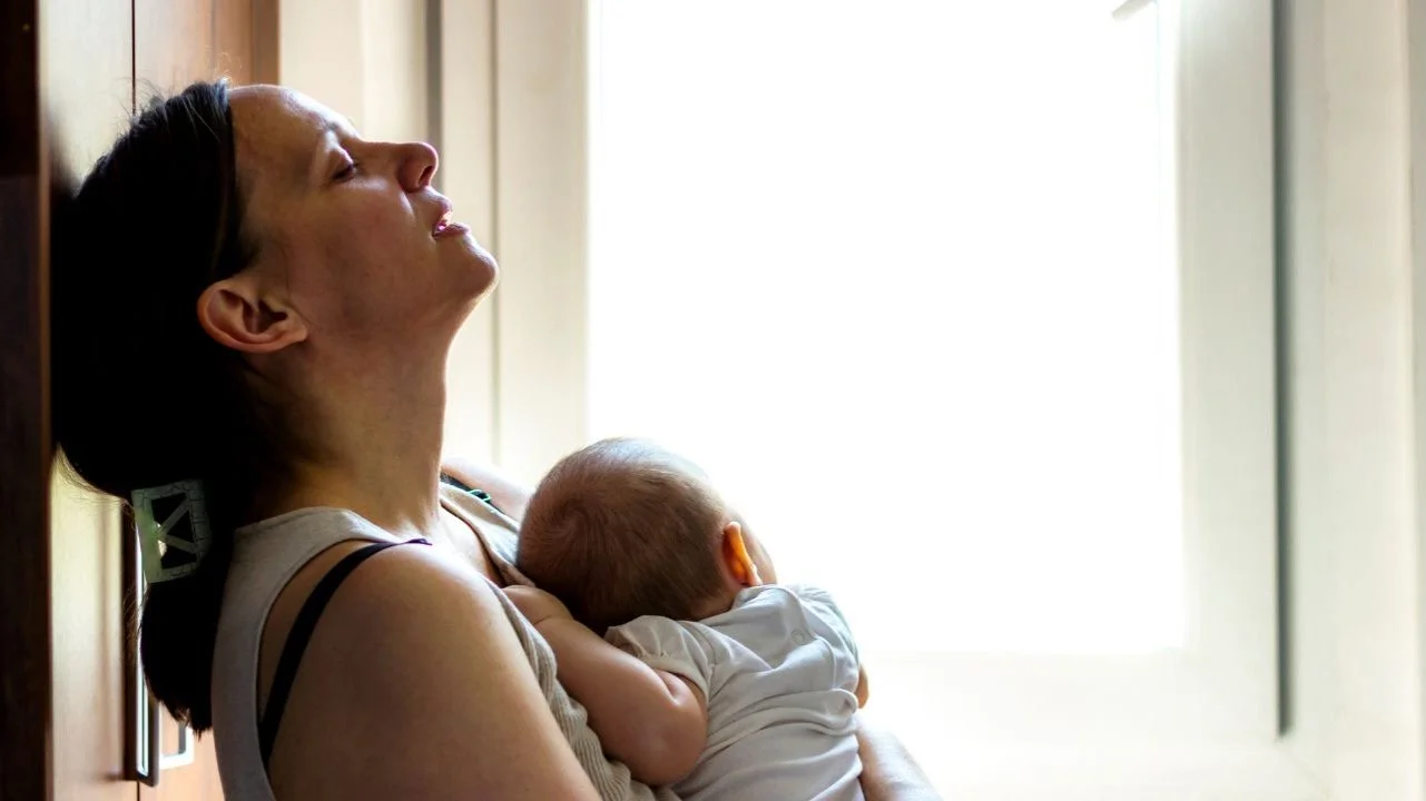 stressed mom leaning against wall holding baby