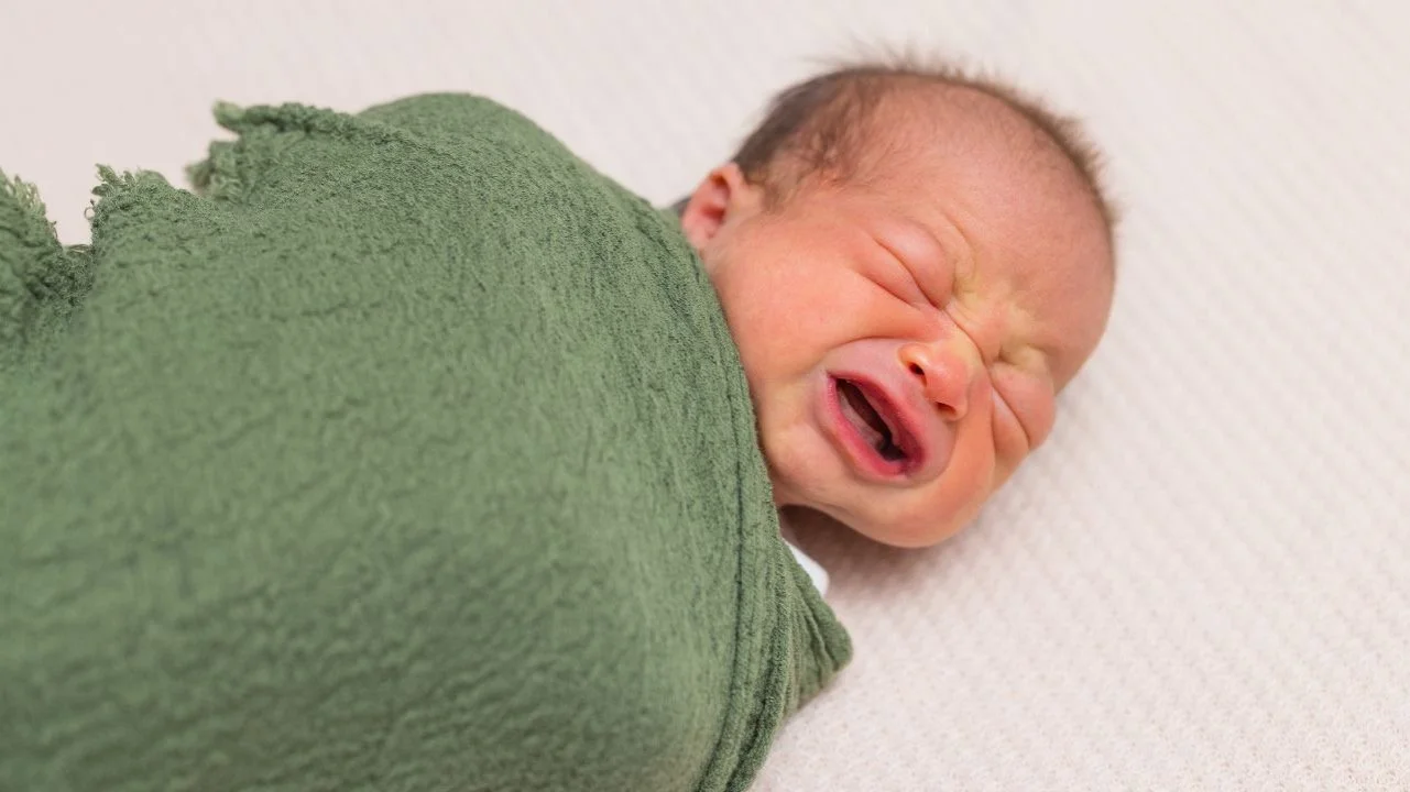 newborn baby in green swaddle crying
