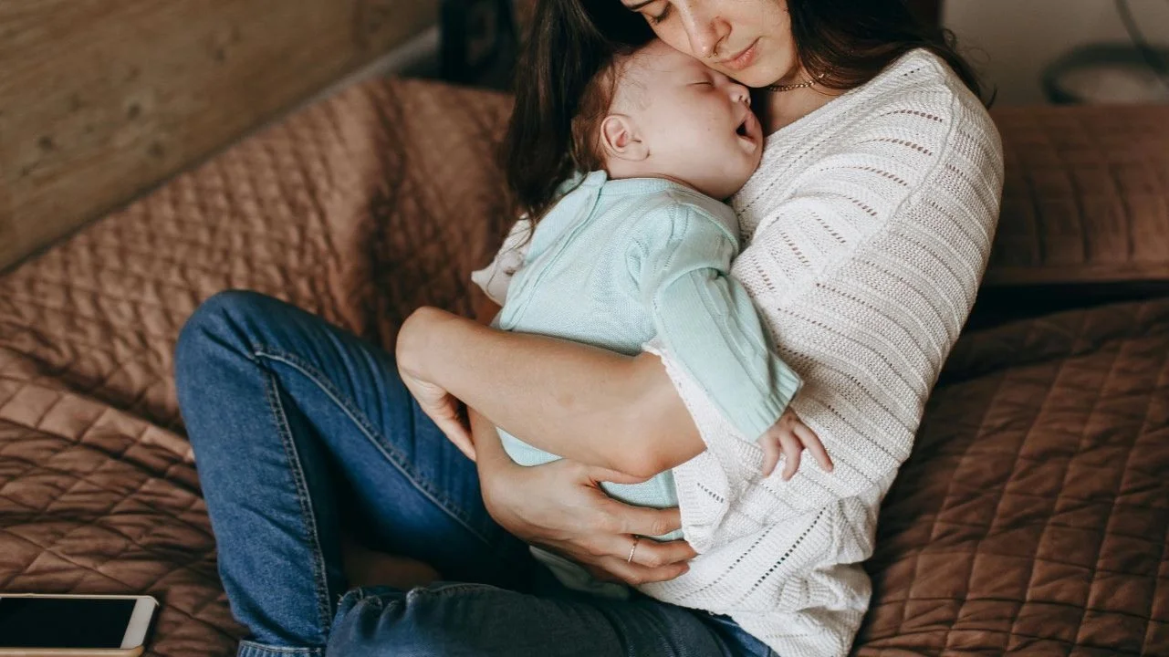 mom holding sleeping baby on her bed