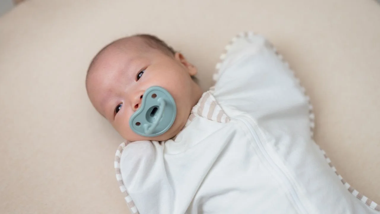 baby in a sleep sack with a pacifier in their mouth