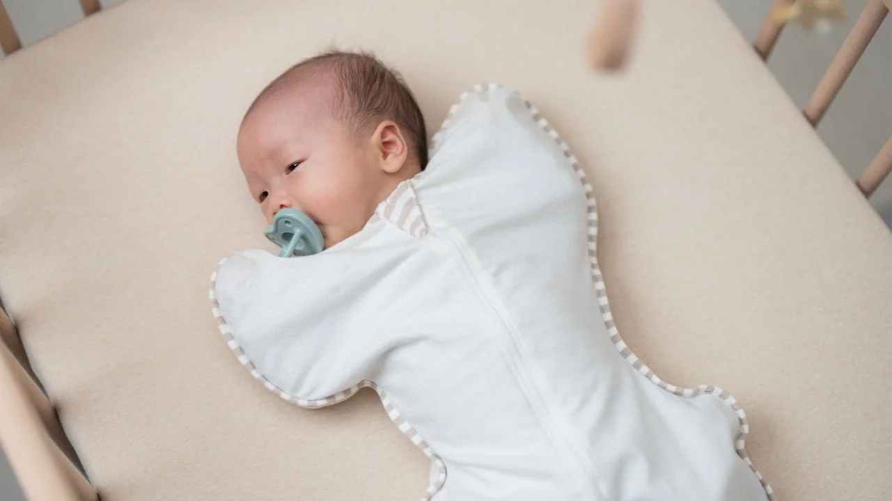 newborn baby in crib with pacifier and swaddle sleep sack on