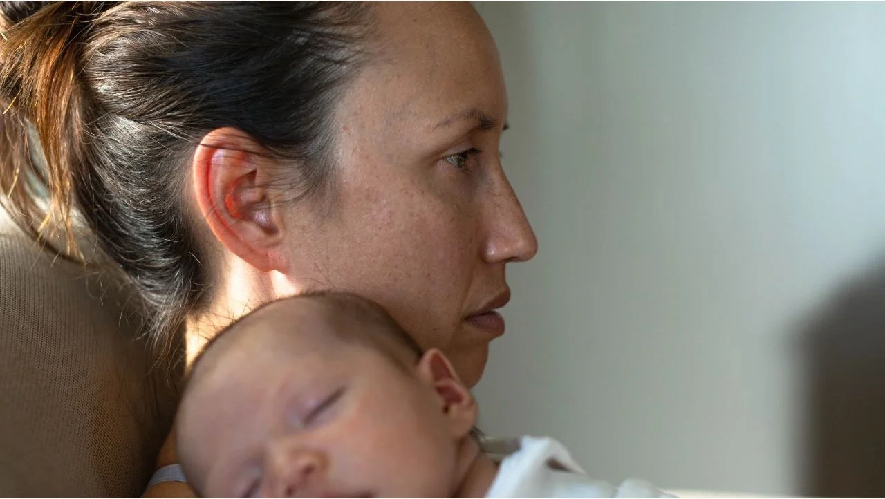 sad looking woman holding a sleeping baby